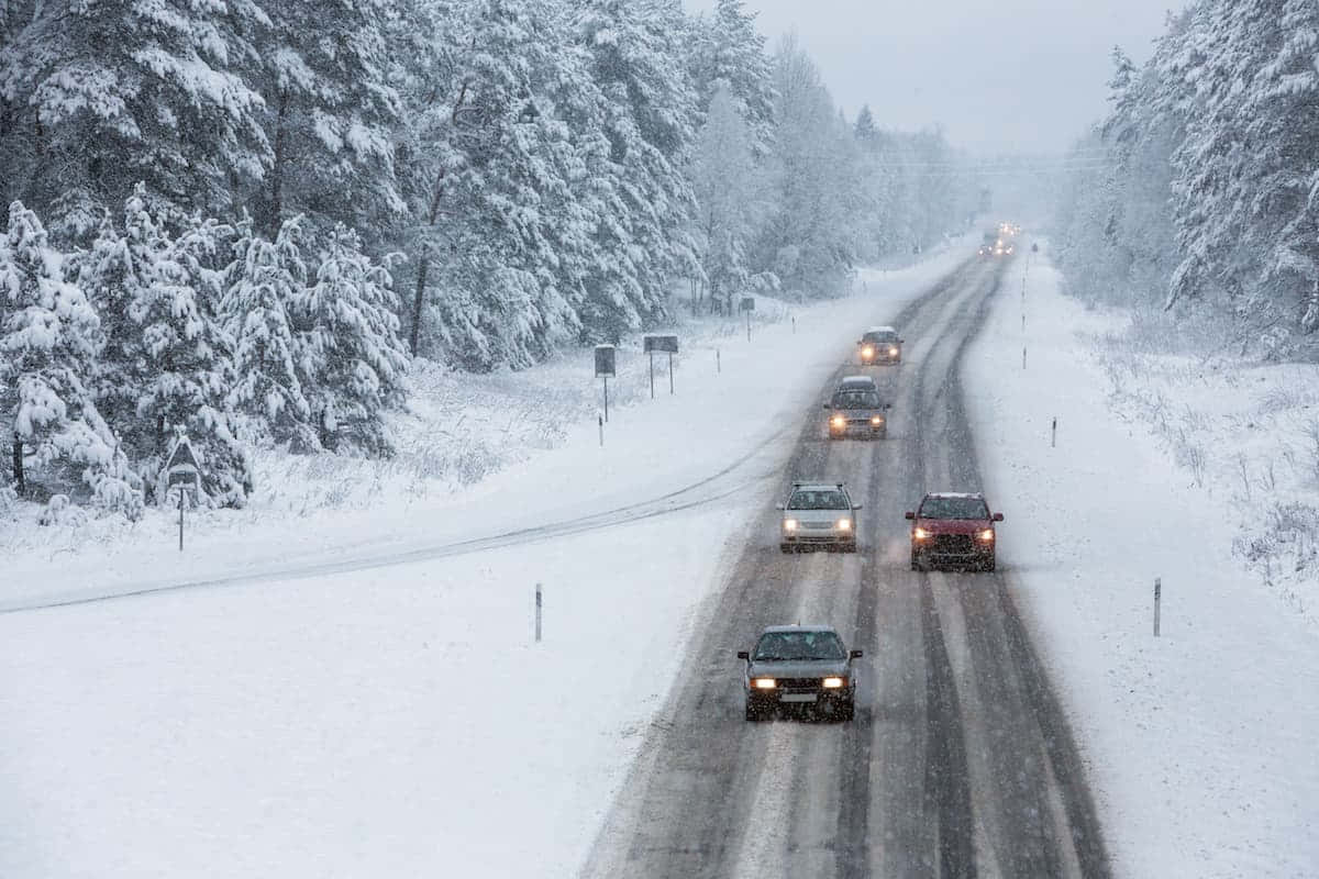 Winter Driving 桌布 壁紙 — 汽車在白雪覆蓋的森林道路上謹慎行駛，周圍大雪紛飛。