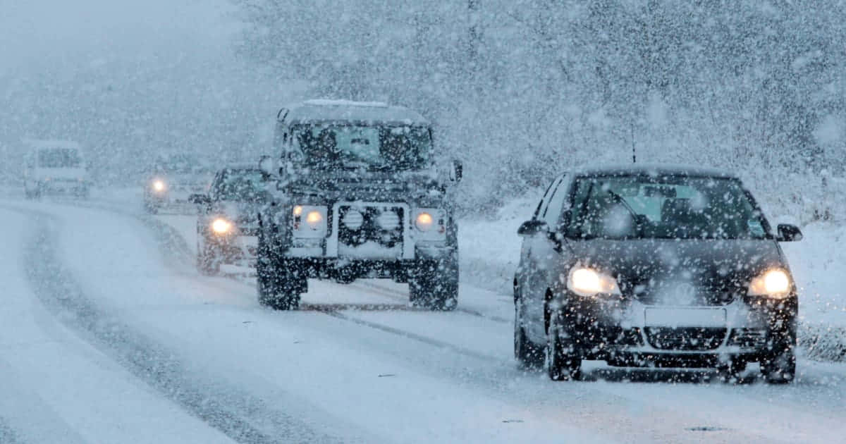 Winter Driving 桌布 壁紙 — 汽車在白雪覆蓋的道路上行駛，大雪紛飛遮蔽了周圍的冬日景觀。