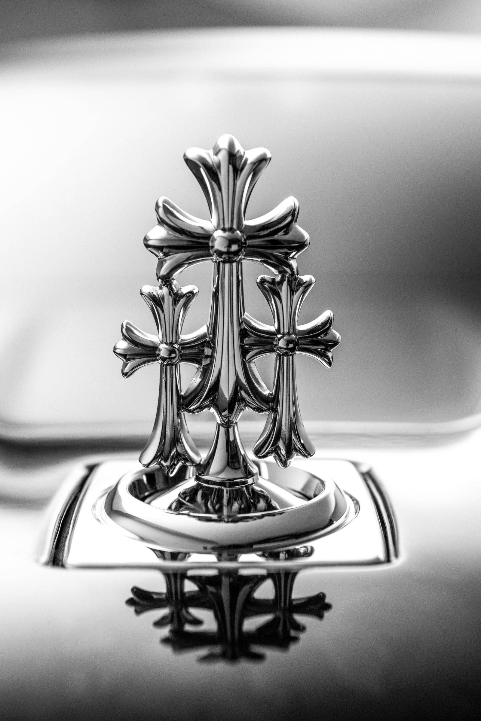 Chrome Hearts 桌布 壁紙 — 汽車引擎蓋上鍍鉻十字標誌的單色特寫，具有銳利反射和淺景深。
