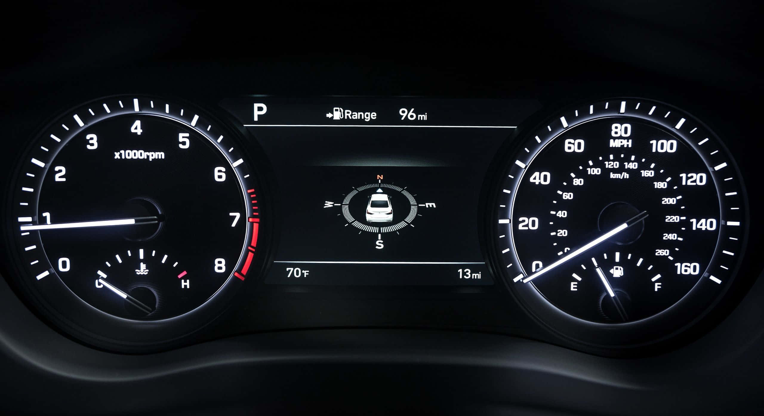 Genesis G80 桌布 壁紙 — 汽車發光儀表板的特寫，顯示速度計、轉速計和數位顯示屏，並帶有停車檔和續航里程指示器。