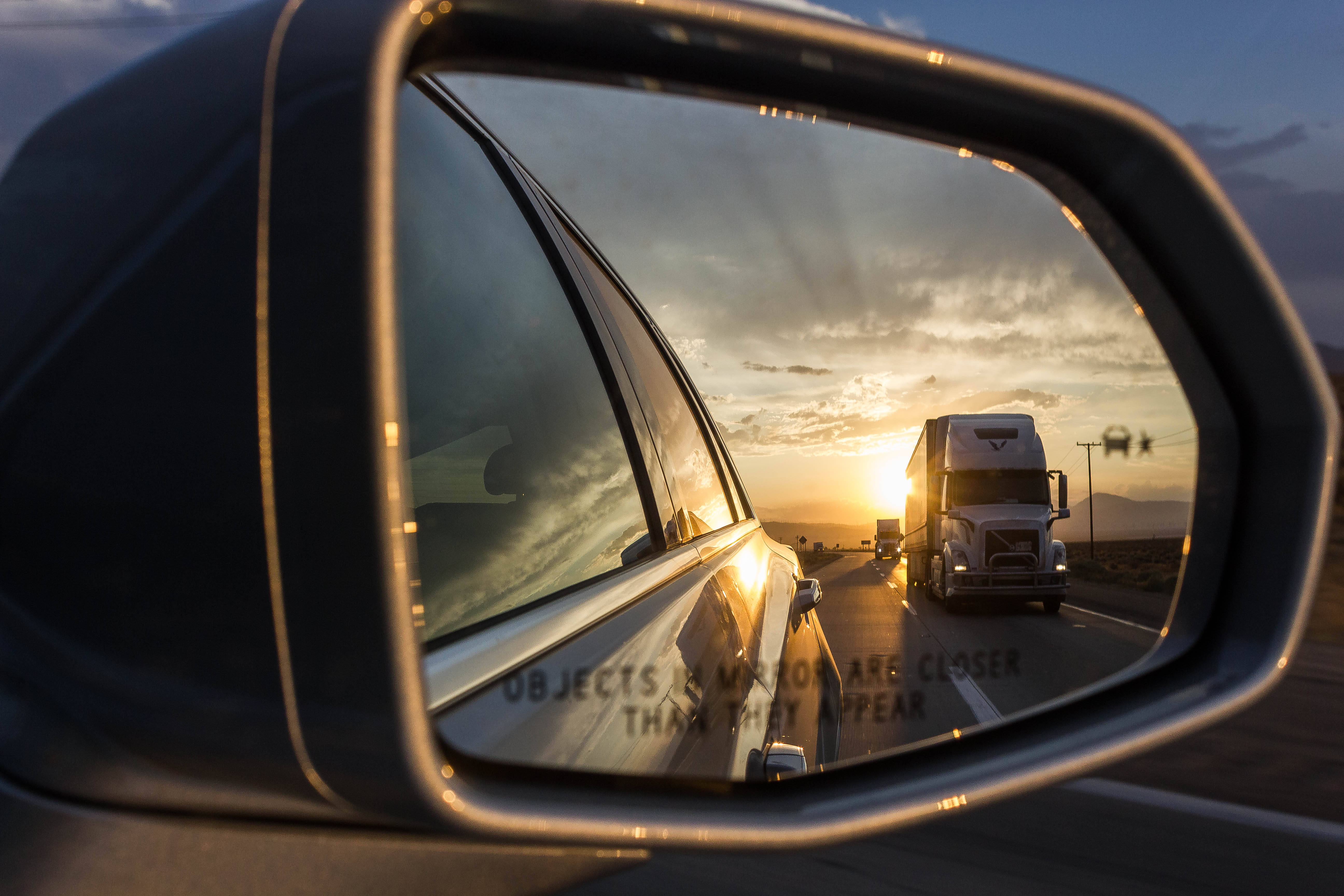 Truck 桌布 壁紙 — 汽車的側鏡反射出在沙漠公路上夕陽西下時，一輛半掛卡車在溫暖的金色光芒中駛近。