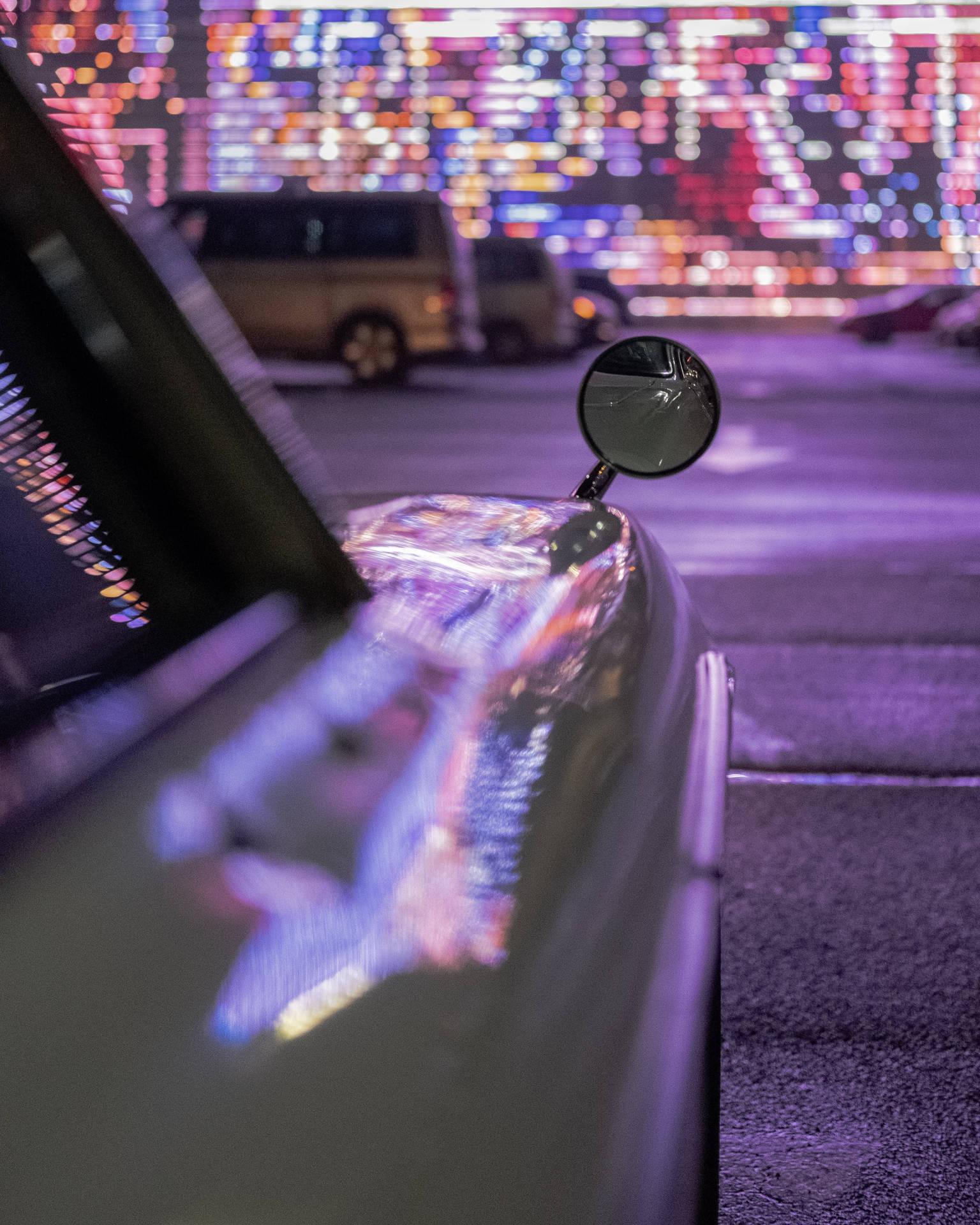 汽車側鏡和引擎蓋在夜晚反射出多彩的城市燈光。