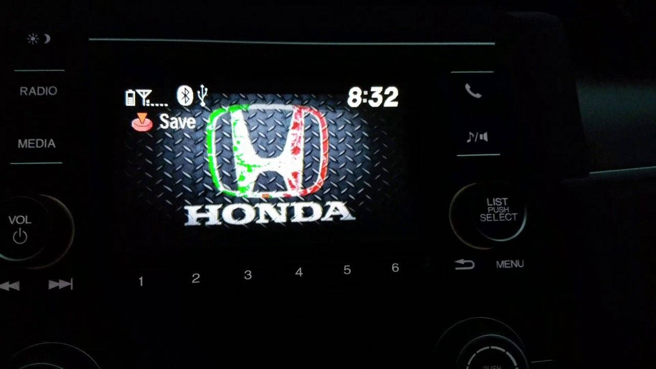 Honda 桌布 壁紙 — 汽車資訊娛樂螢幕的特寫，顯示帶有磨損紋理和發光綠色和紅色點綴的 Honda 標誌，背景為黑暗的車廂。