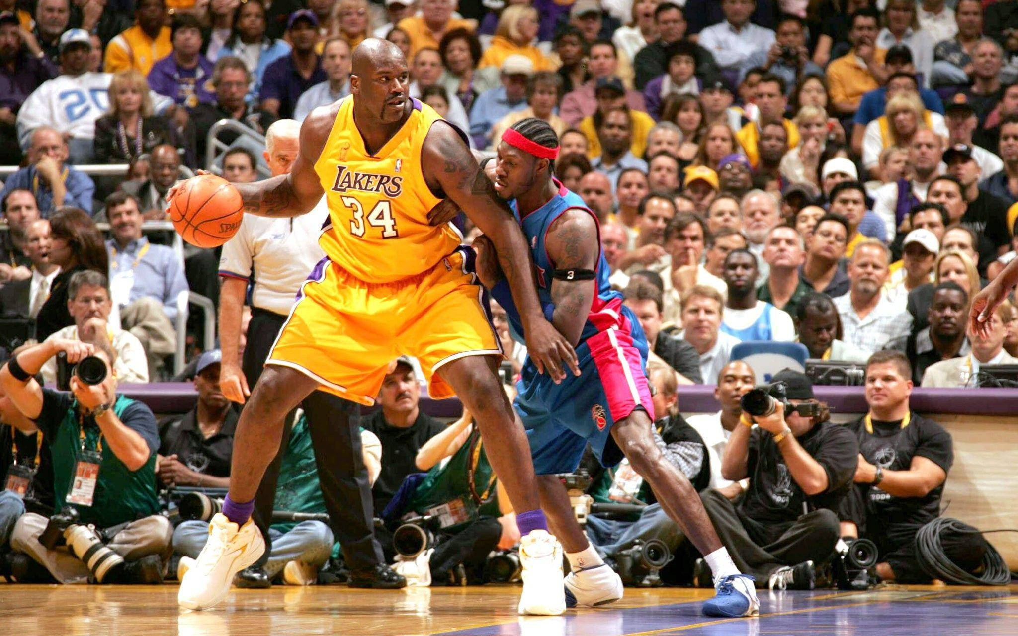 Shaquille O'neal 桌布 壁紙 — 沙奎爾·奧尼爾身穿黃色湖人隊球衣，在激烈的比賽中運球，同時被身穿藍紅相間球衣的對手防守。