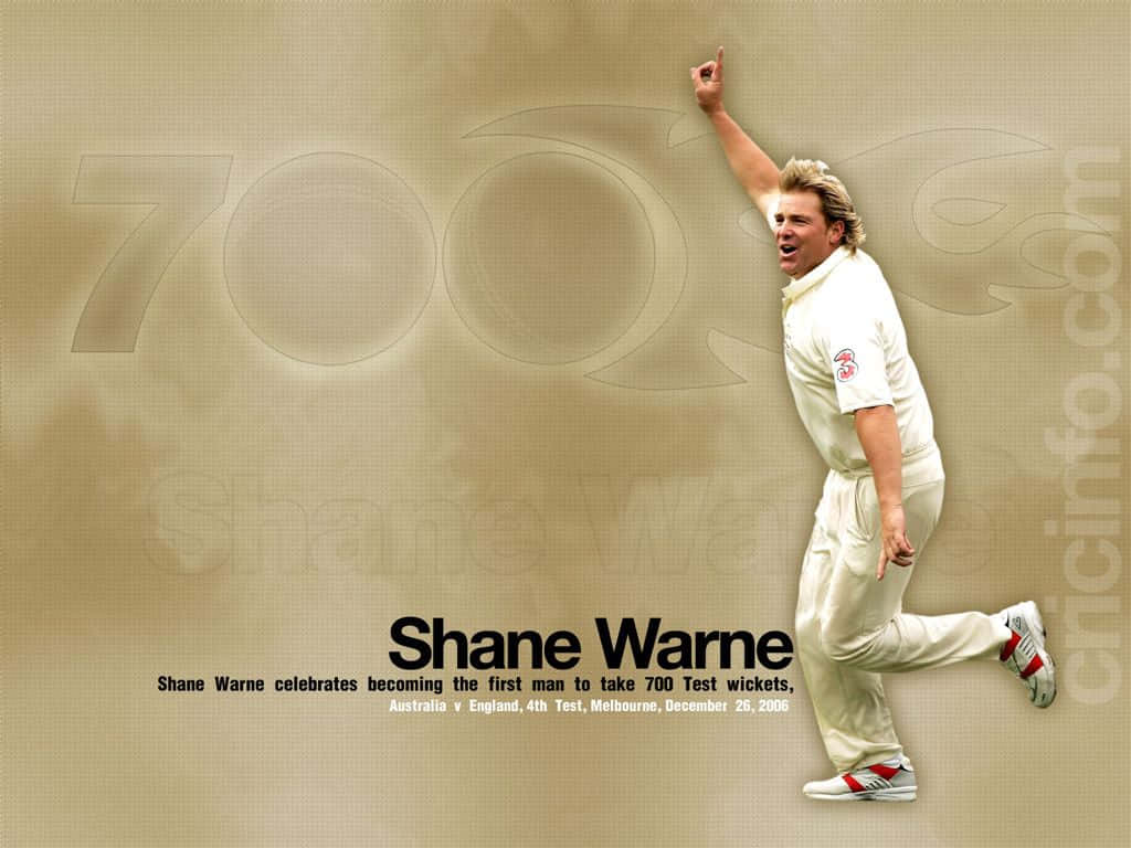 Shane Warne 桌布 壁紙 — 沙恩·沃恩身穿白色板球服，在米色背景上舉臂歡呼，背景有模糊的「700」字樣。