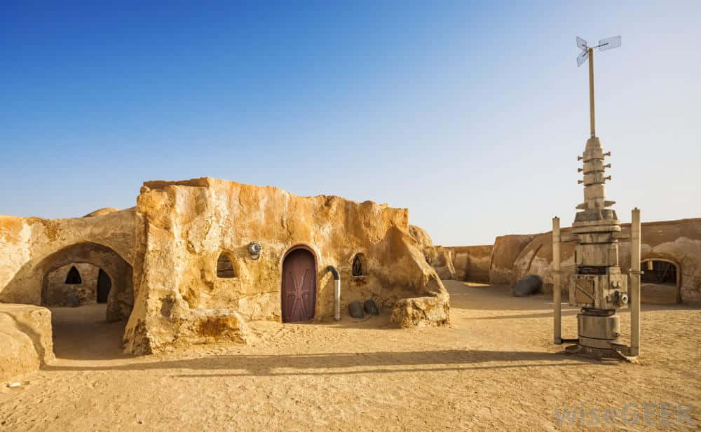 Mos Eisley 桌布 壁紙 — 沙漠星球上的家園，有沙石住宅和一個高高的風向標，在清澈的藍天下。