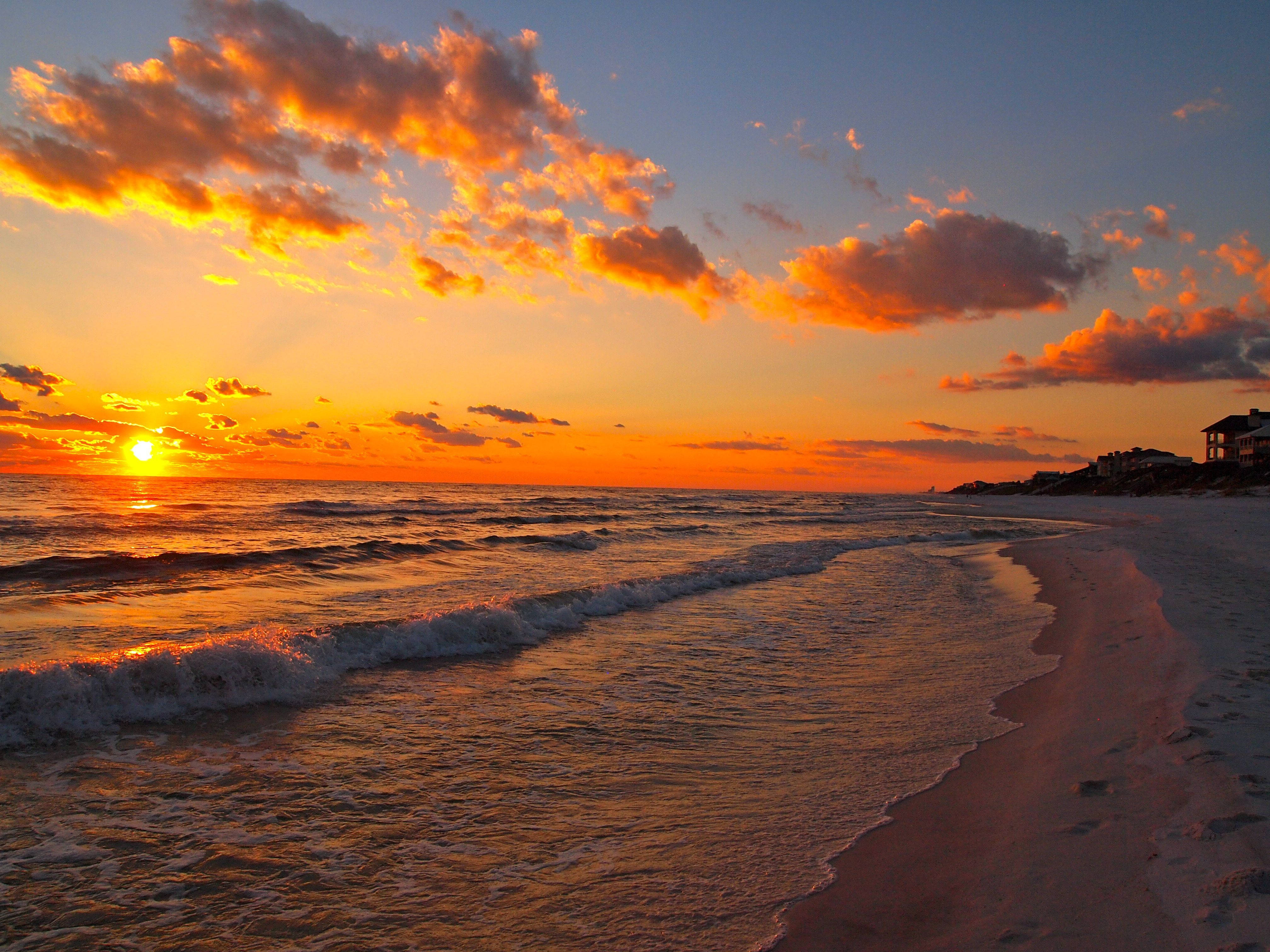 Beach Sunset 桌布 壁紙 — 沙灘上波濤洶湧，橙色雲彩在地平線上空閃耀，令人嘆為觀止的日落。