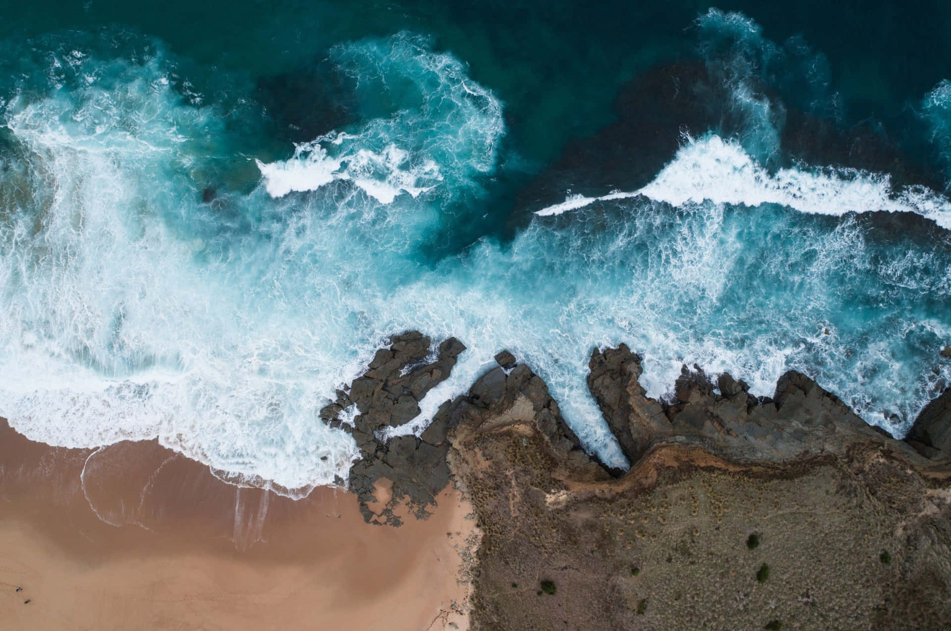 翠綠色海浪從上方拍打沙灘旁的黑暗懸崖。 — Google pixel 壁紙