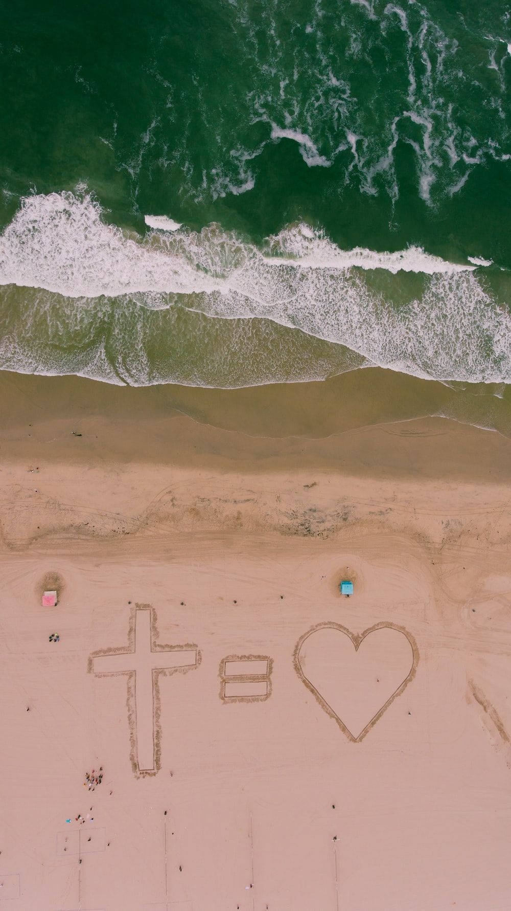 Jesus Aesthetic 桌布 壁紙 — 沙灘的鳥瞰圖，沙灘上畫著一個十字等於一顆心，旁邊是破碎的綠色海浪。