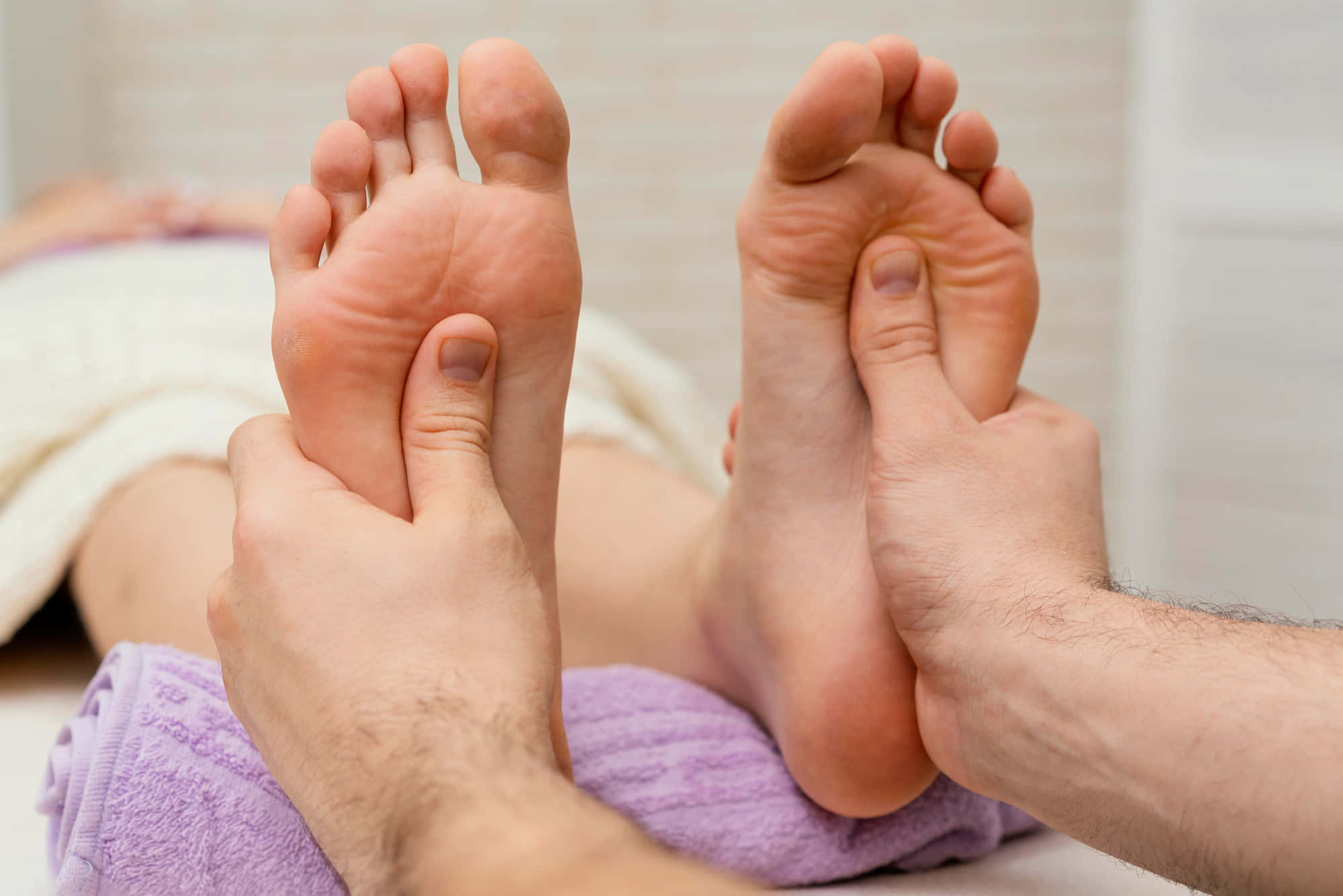 Massage 桌布 壁紙 — 治療師雙手在紫色毛巾上為客戶按摩赤裸雙腳的水療中心特寫。