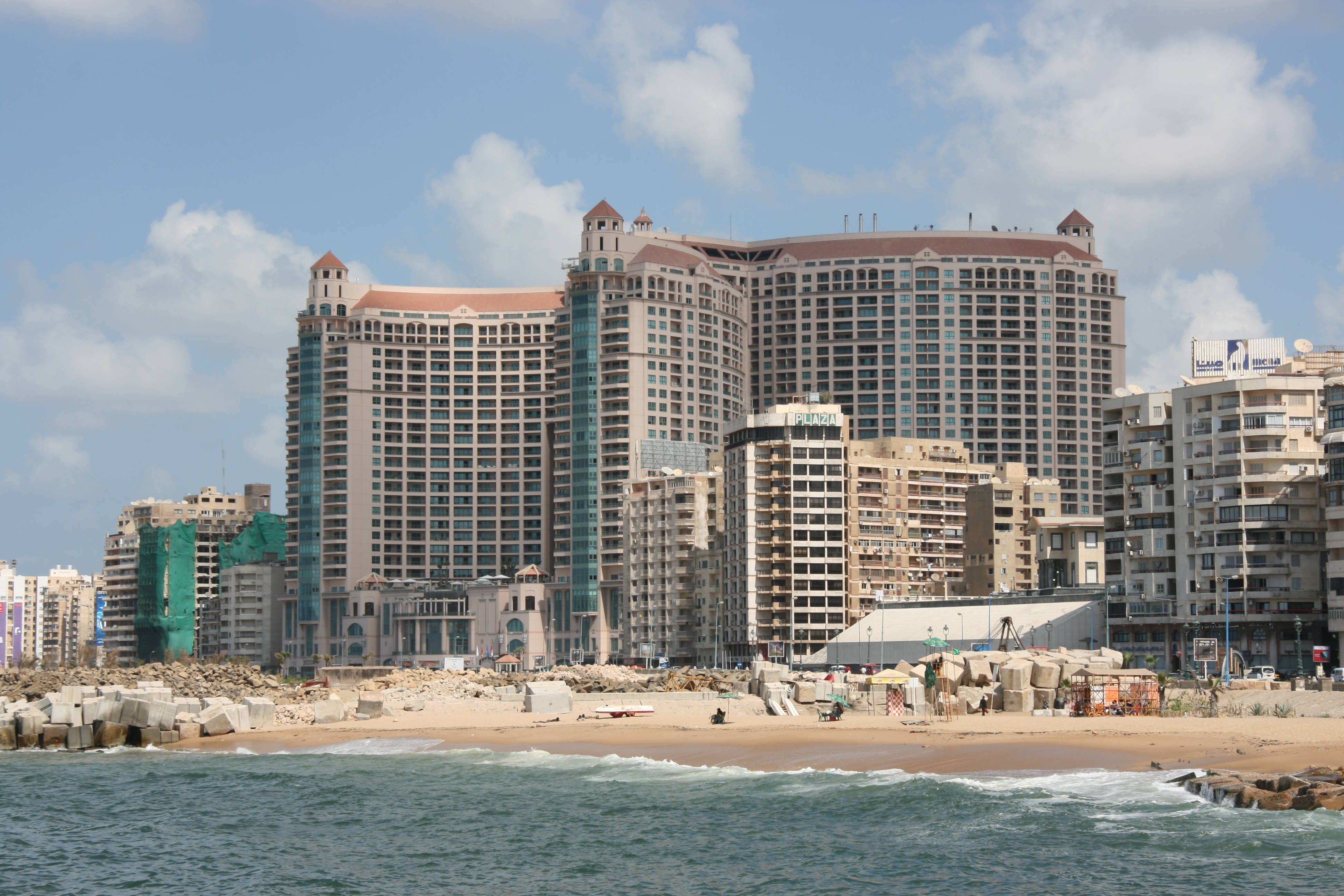 Alexandria 桌布 壁紙 — 沿海城市景觀，沙灘旁高聳的飯店和建築物林立，天空湛藍，白雲點點。
