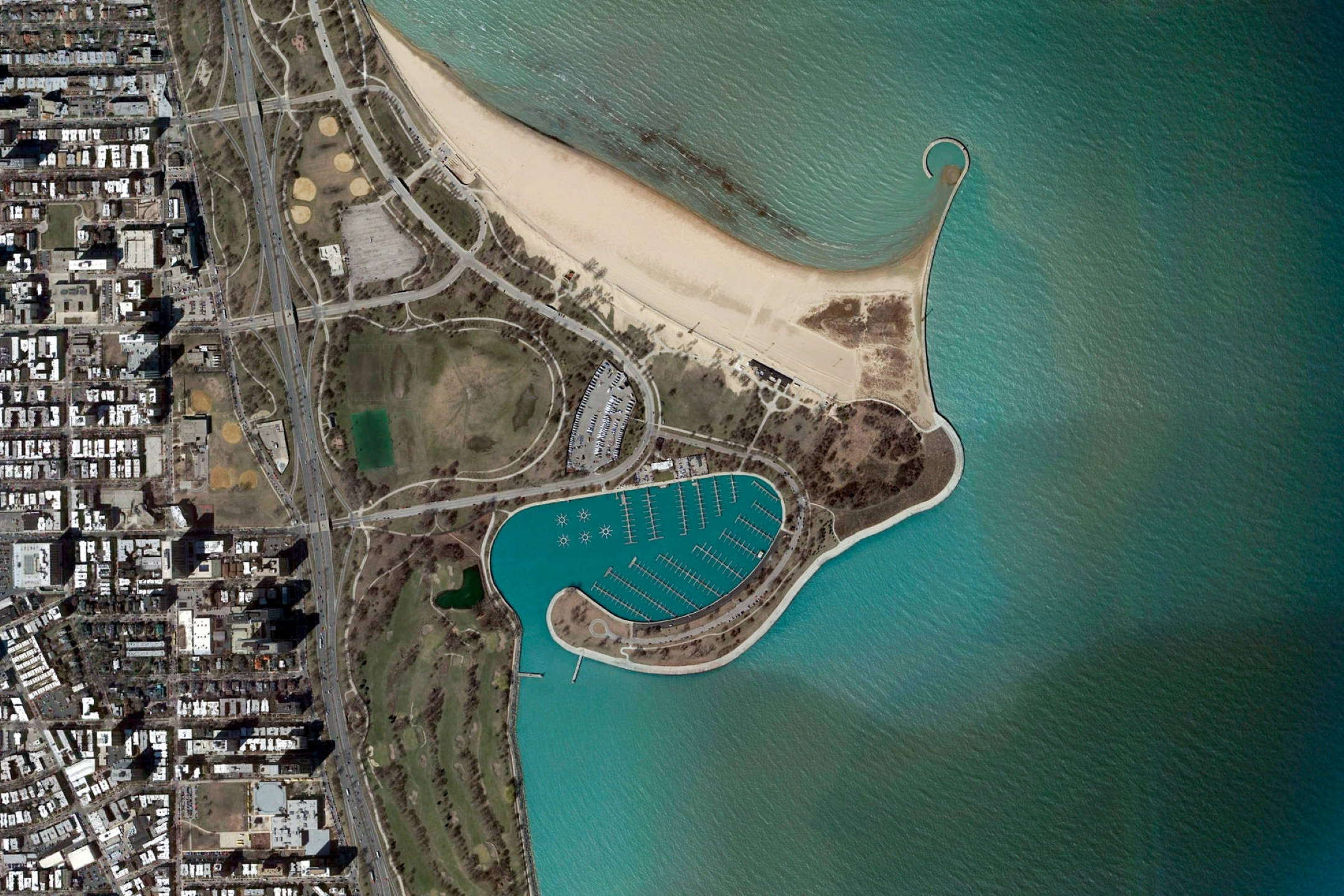 Google 地球 桌布 壁紙 — 沿海城市景觀的鳥瞰圖，擁有彎曲的沙灘、藍綠色碼頭以及與水相接的城市網格。
