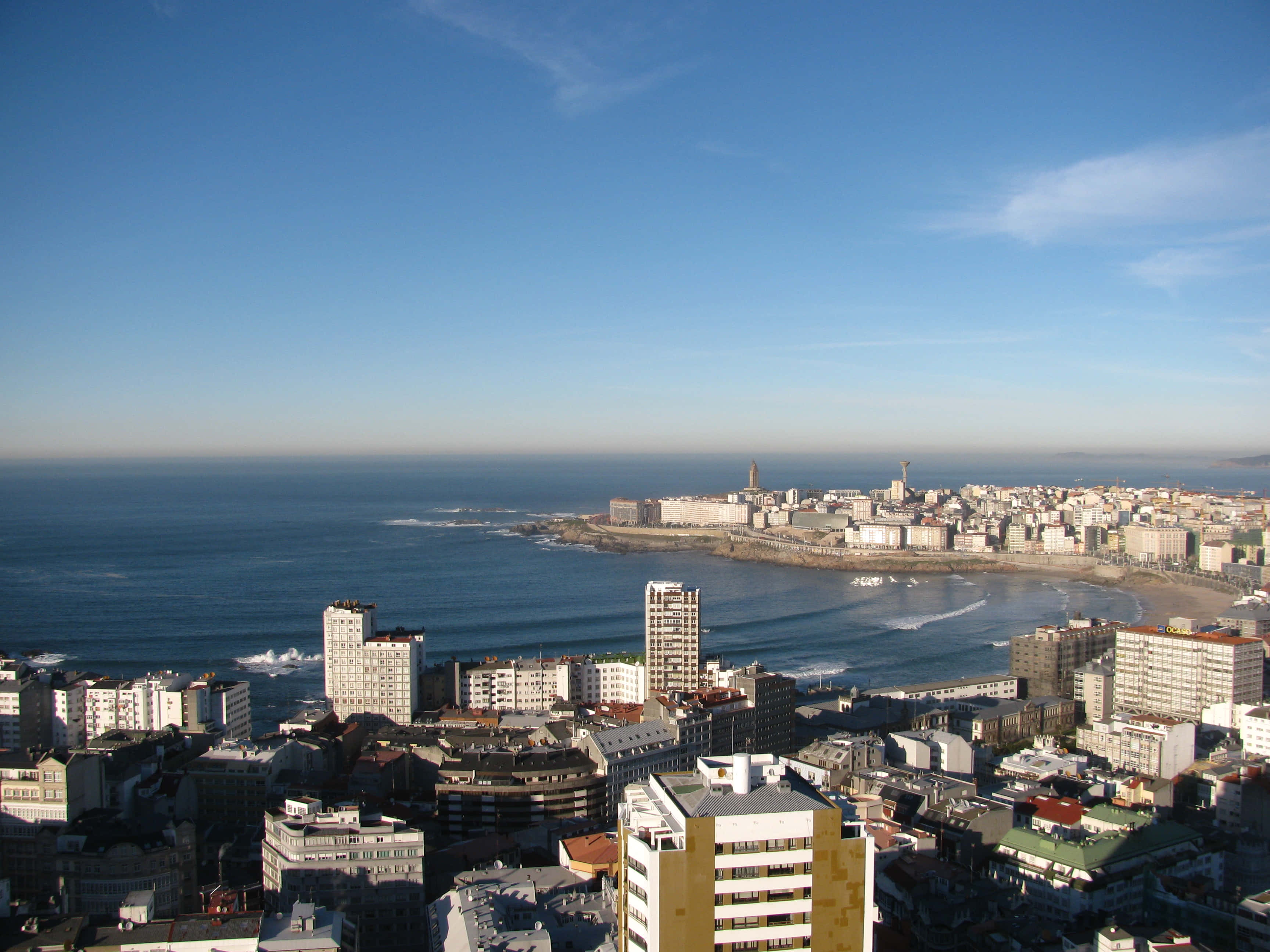 Blue Sky Aesthetic 桌布 壁紙 — 沿海城市的鳥瞰圖，現代建築擁抱著海岸線，天空清澈湛藍。