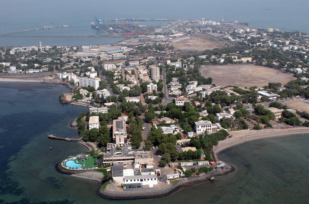 水 桌布 壁紙 — 沿海城鎮的鳥瞰圖，建築物坐落在碧綠海水與遠處的大型工業港口之間。