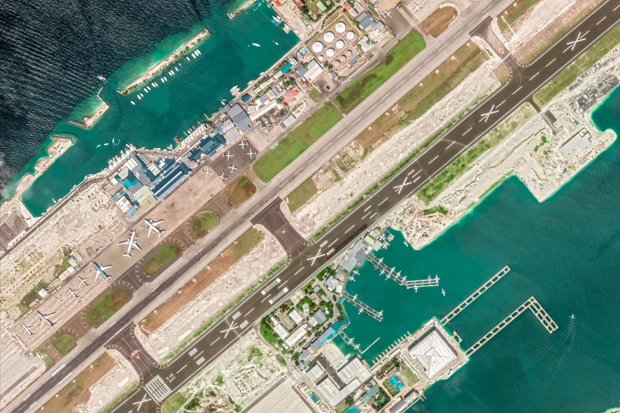 Google 地球 桌布 壁紙 — 沿海機場的鳥瞰圖，跑道、飛機以及圍繞航廈和碼頭的碧綠海水。