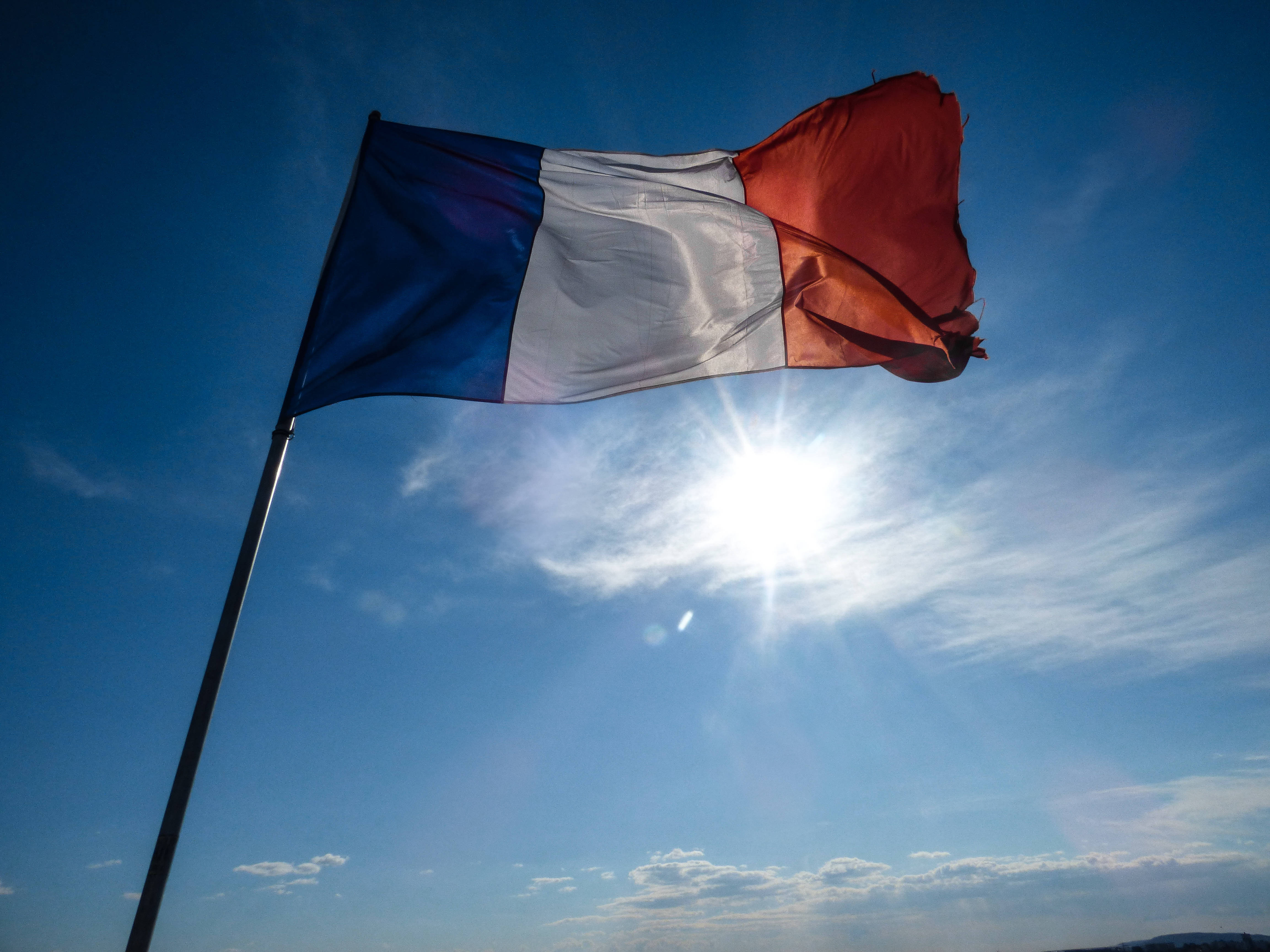 France Flag 桌布 壁紙 — 法國國旗在明亮的藍天下自豪地飄揚，陽光穿透旗幟。