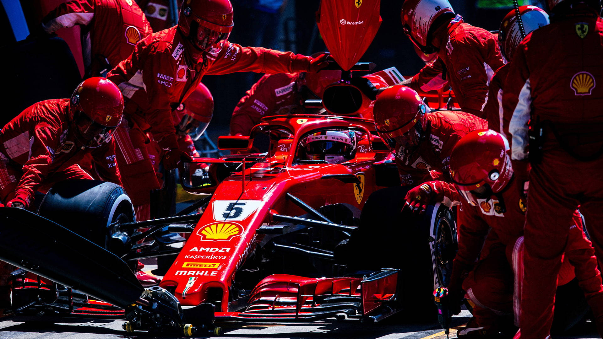 F1 桌布 壁紙 — 法拉利F1車隊維修人員身穿紅色制服，在明亮的賽道燈光下迅速為5號賽車更換輪胎。