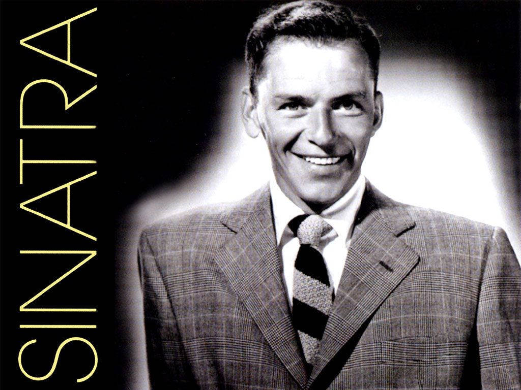 Sinatra 桌布 壁紙 — 法蘭克·辛納屈穿著格紋西裝，在聚光燈背景下溫暖微笑的經典黑白肖像。