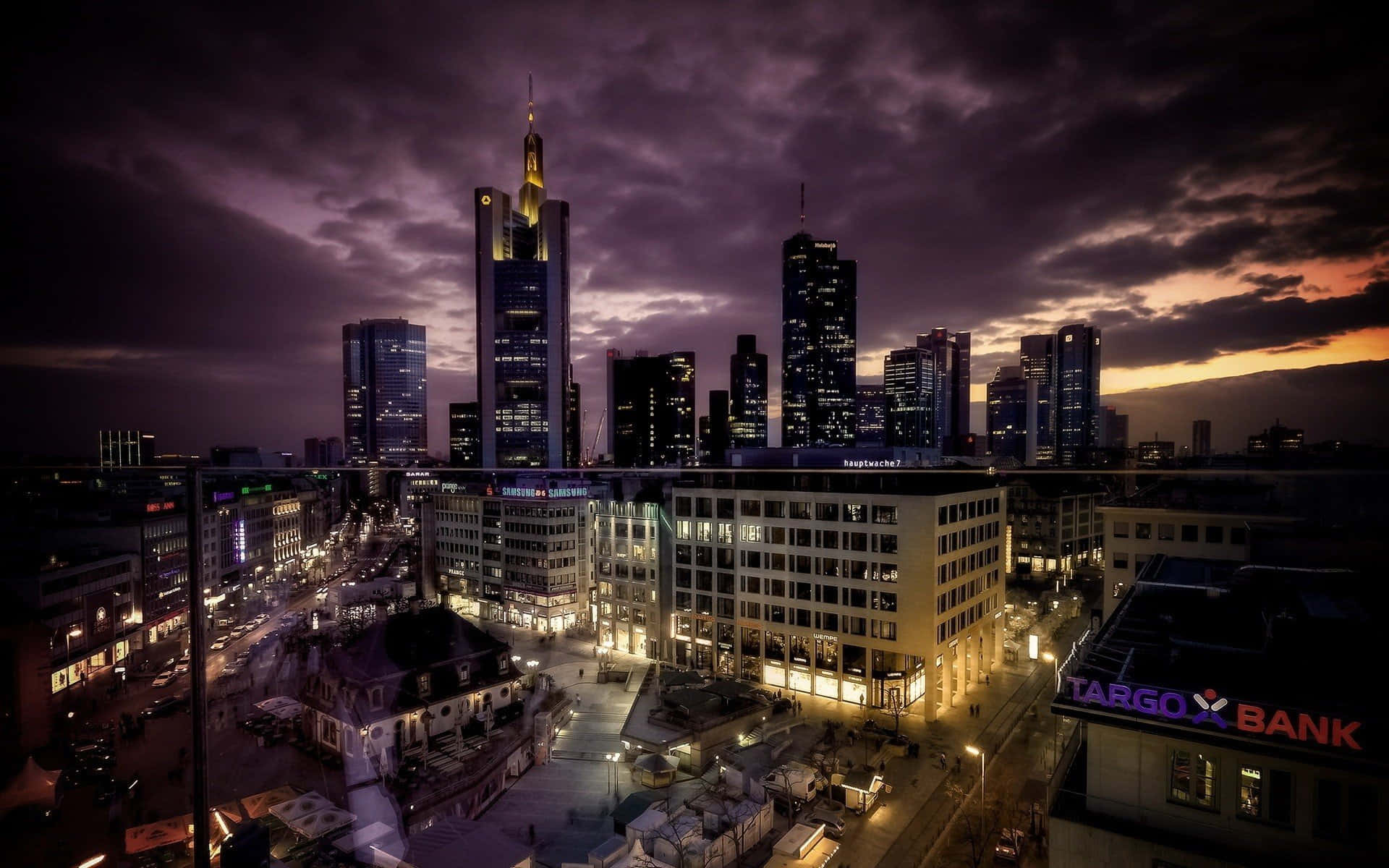 德國 桌布 壁紙 — 法蘭克福戲劇性的黃昏城市景觀，摩天大樓在紫色和橙色的天空下閃耀著燈光。