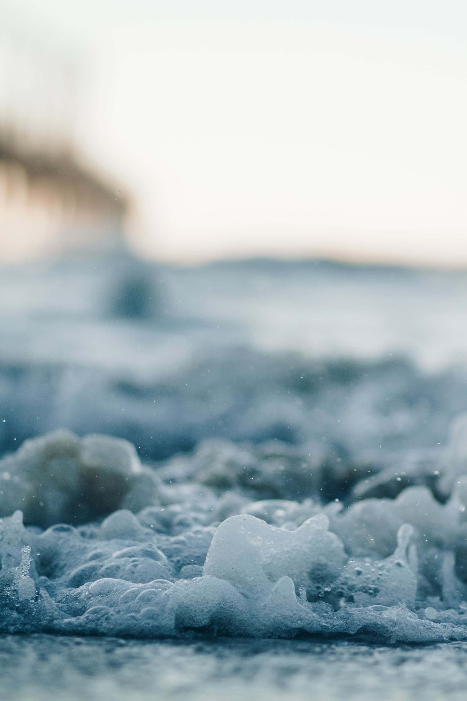 Beach Aesthetic 桌布 壁紙 — 泡沫海浪拍打沙灘的特寫，背景有柔和模糊的碼頭。