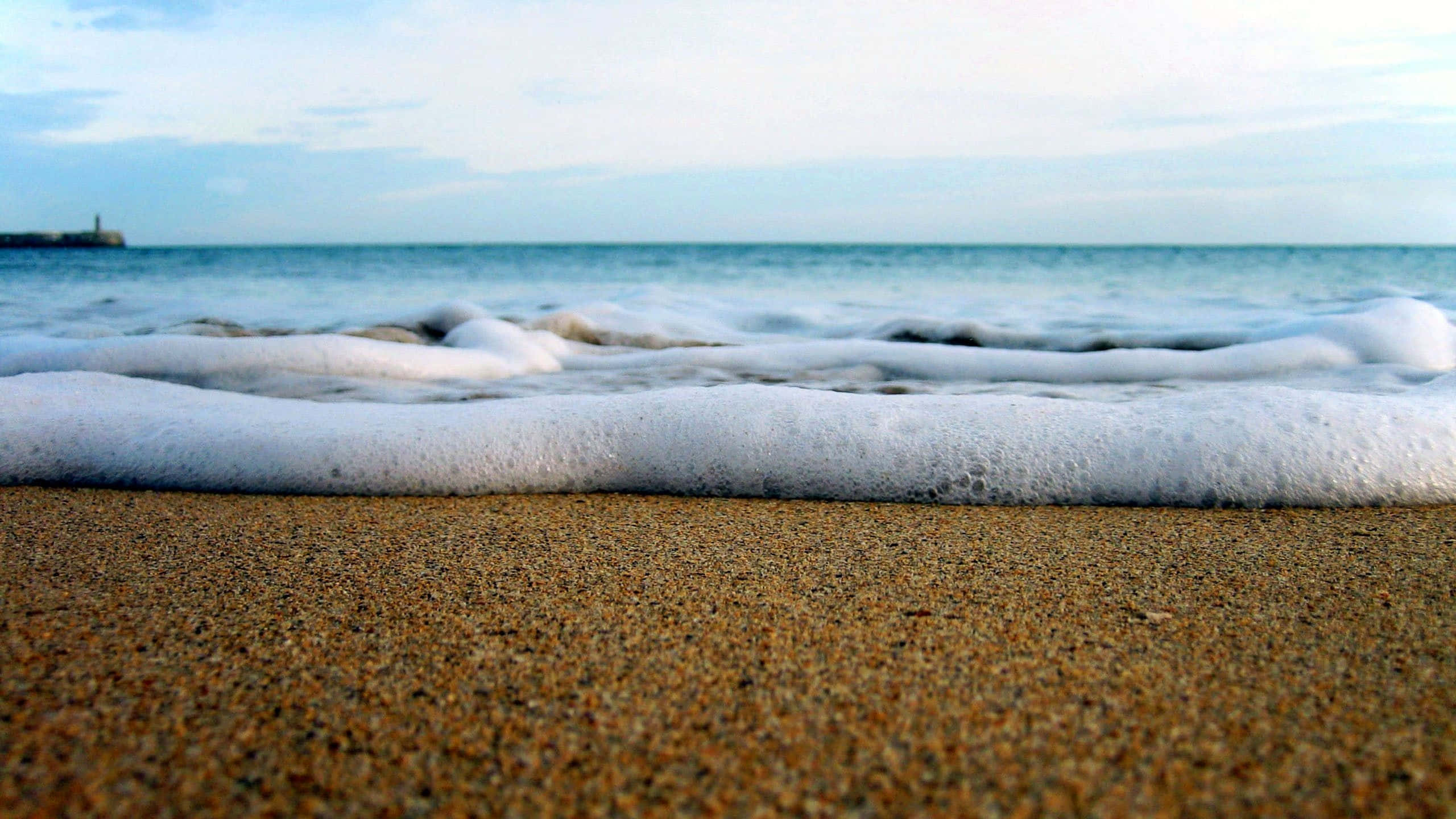 Ocean Waves 桌布 壁紙 — 泡沫海浪輕輕拍打著質感豐富的金色沙灘，天空柔和湛藍。