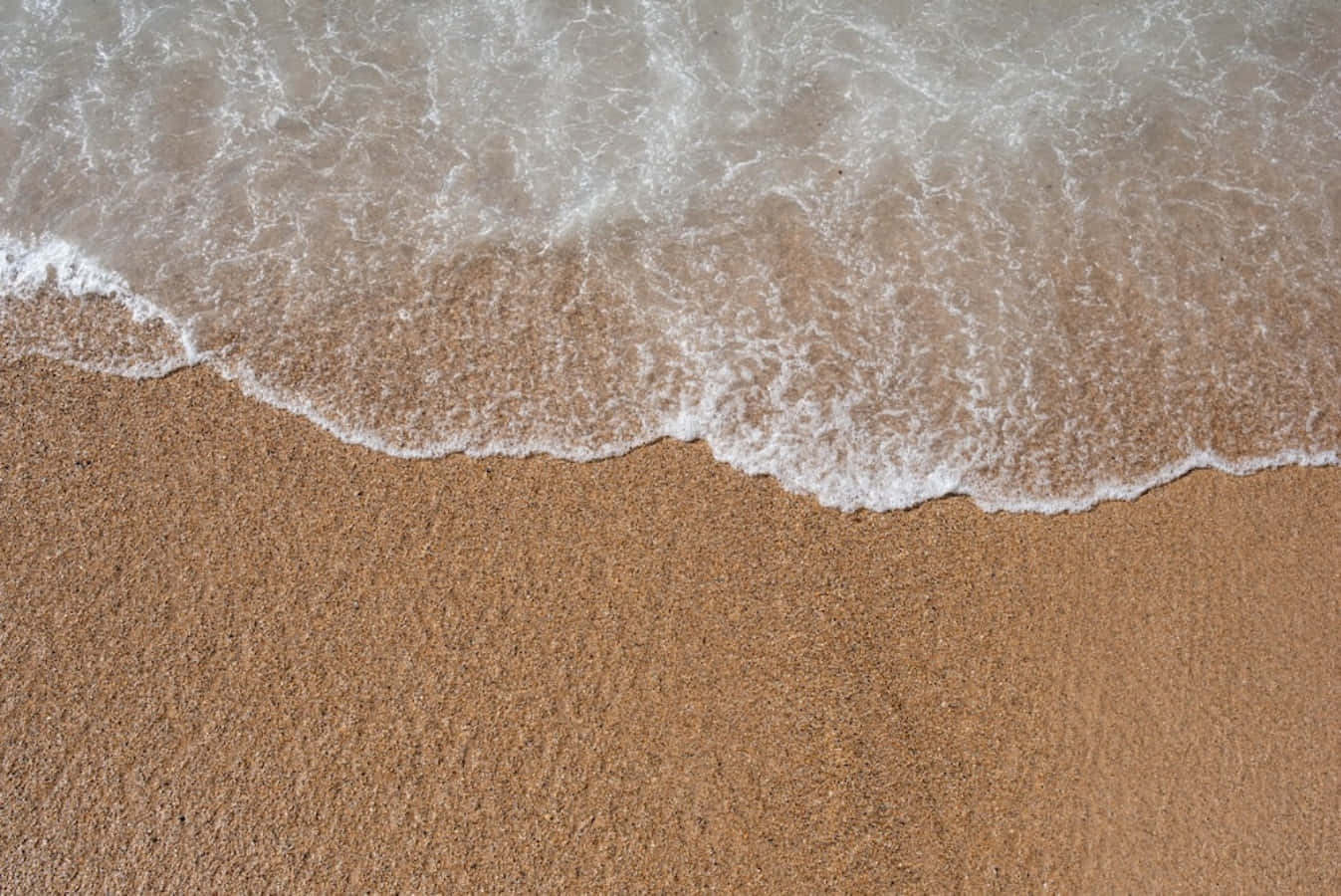 sand 桌布 壁紙 — 泡沫狀的海浪輕輕地滾上紋理豐富的金色沙灘，呈現寧靜的海岸景象。