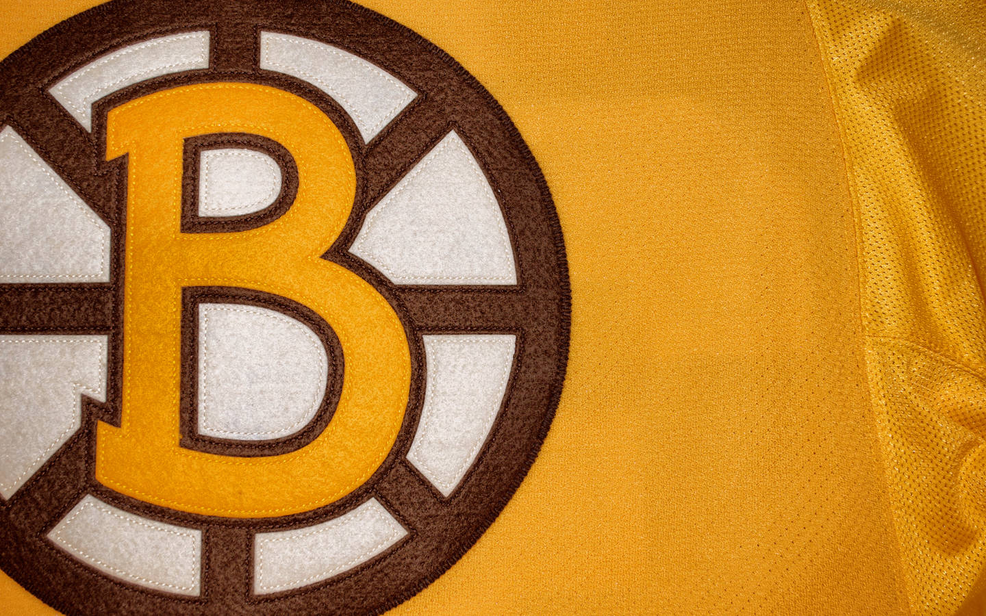 bruins 桌布 壁紙 — 波士頓棕熊隊冰球球衣標誌特寫，在紋理布料上有大膽的黃色、棕色和白色刺繡。