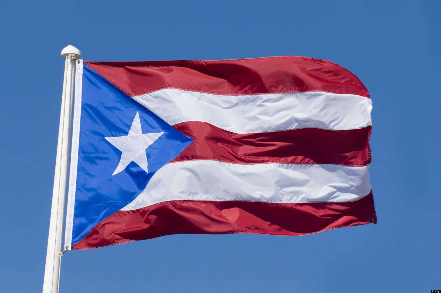 Puerto Rican 桌布 壁紙 — 波多黎各旗幟在清澈的藍天下自豪地飄揚，帶有鮮明的紅、白、藍色彩。