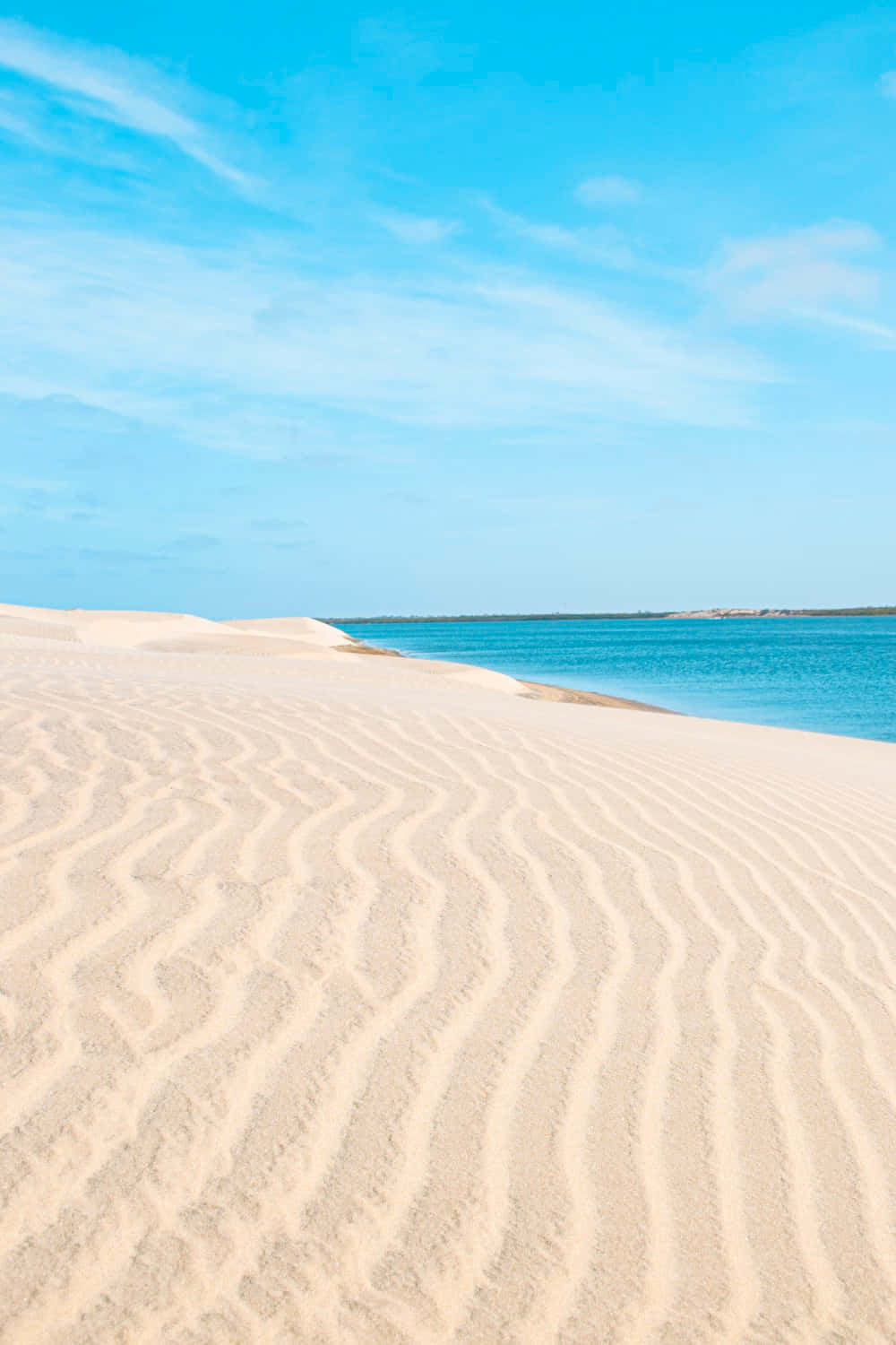 sand 桌布 壁紙 — 波浪狀沙丘在明亮藍天與薄雲下與碧綠海洋交匯。