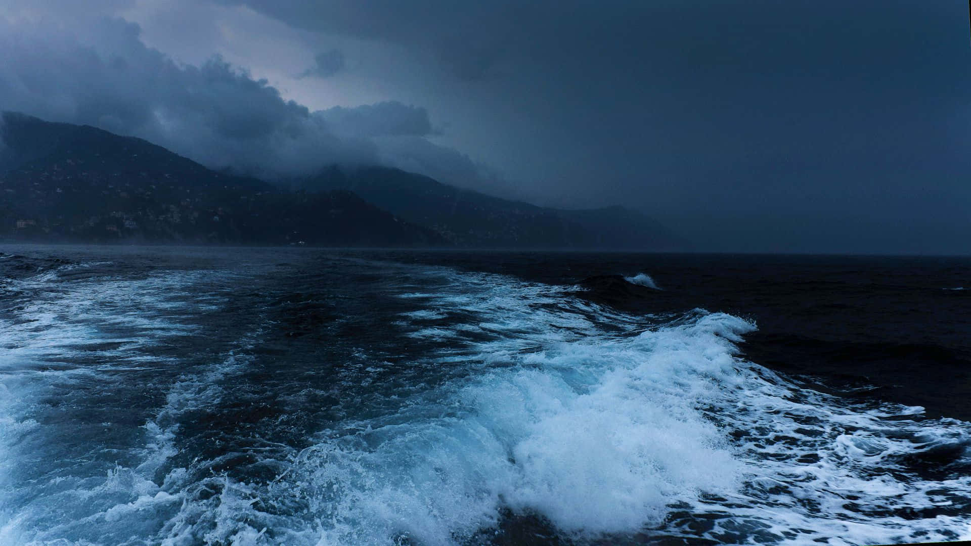 海洋 桌布 壁紙 — 波濤洶湧的大海翻騰著白色泡沫，拍打著陰暗多山的海岸線，天空烏雲密佈。