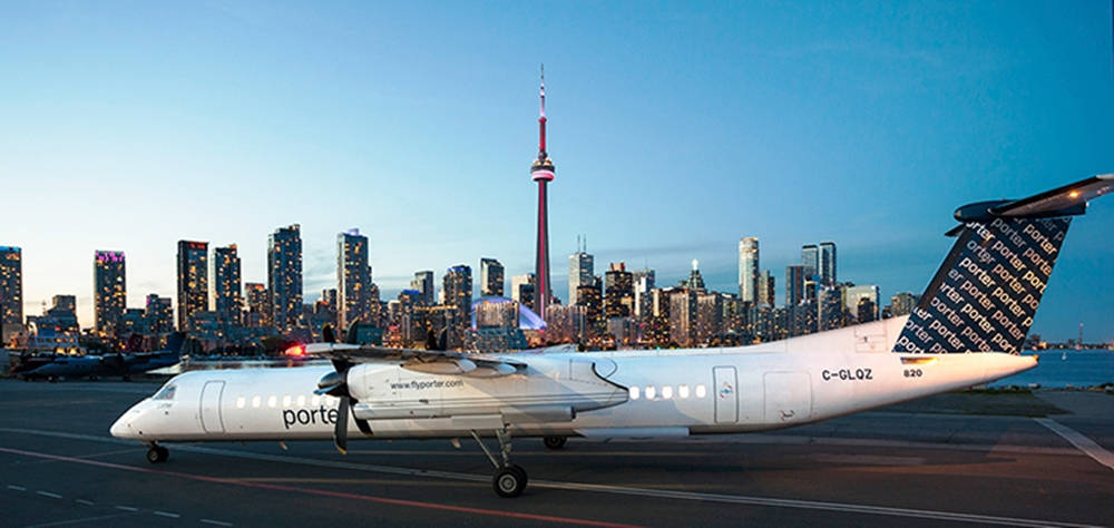 Airport 桌布 壁紙 — 波特航空的一架區域噴射機在機場停機坪滑行，背後是燈火通明的多倫多天際線和CN塔在黃昏中閃耀。