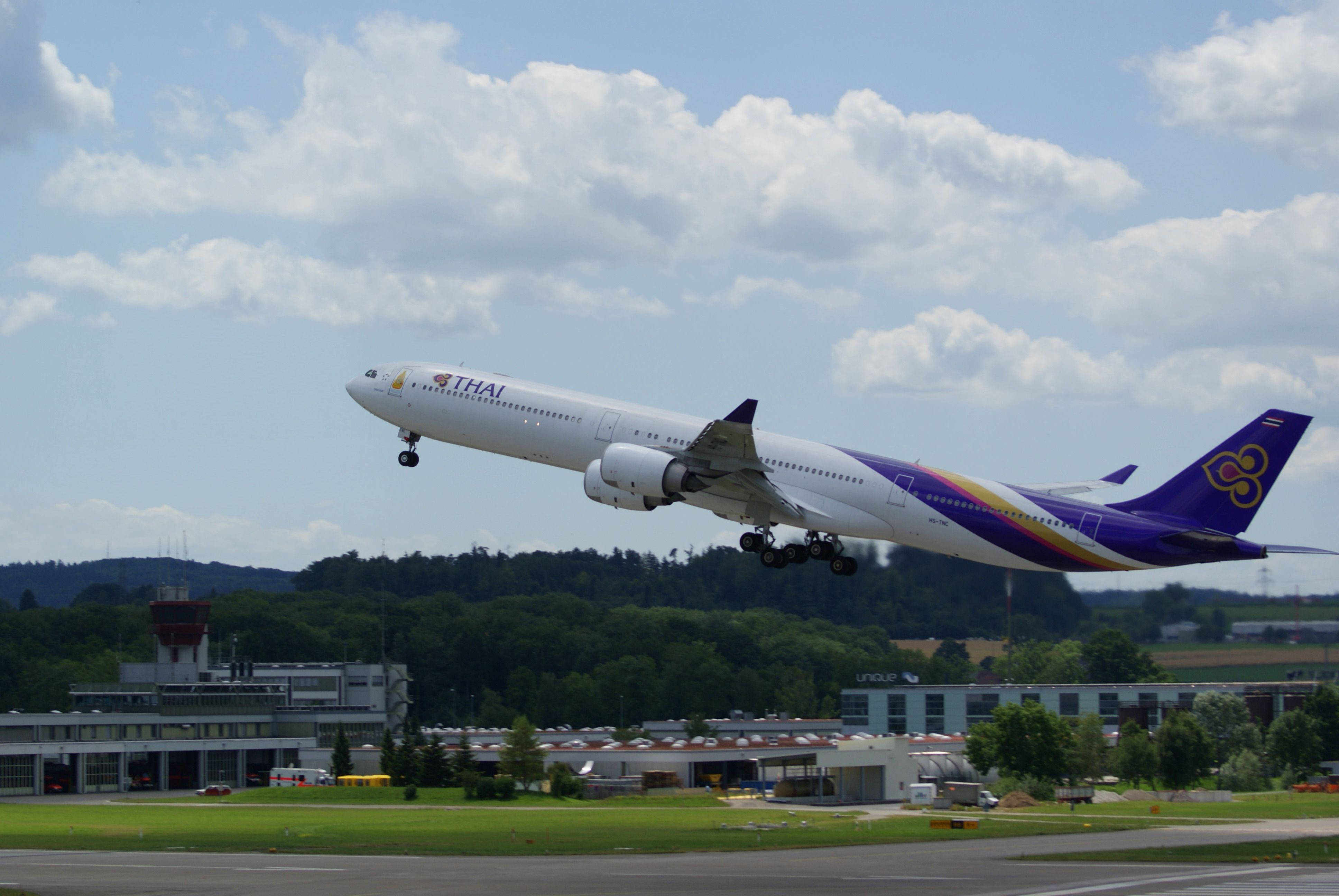 飛機 桌布 壁紙 — 泰國航空的空中巴士A330從跑道起飛，上方有雲，下方有機場建築物。