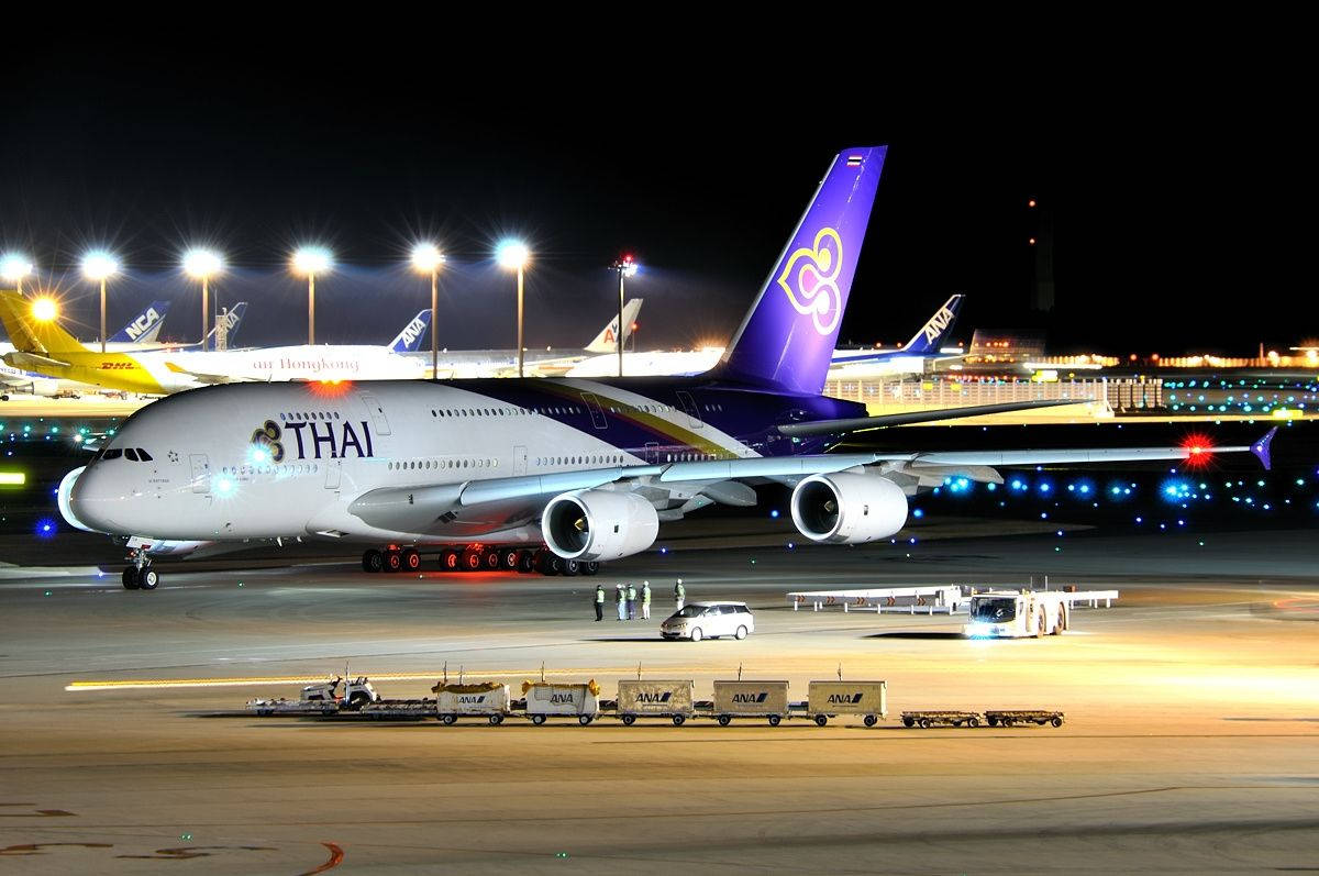 Airport 桌布 壁紙 — 泰國航空的空中巴士A380在夜間於機場停機坪上被照亮，附近有地勤人員和行李車。