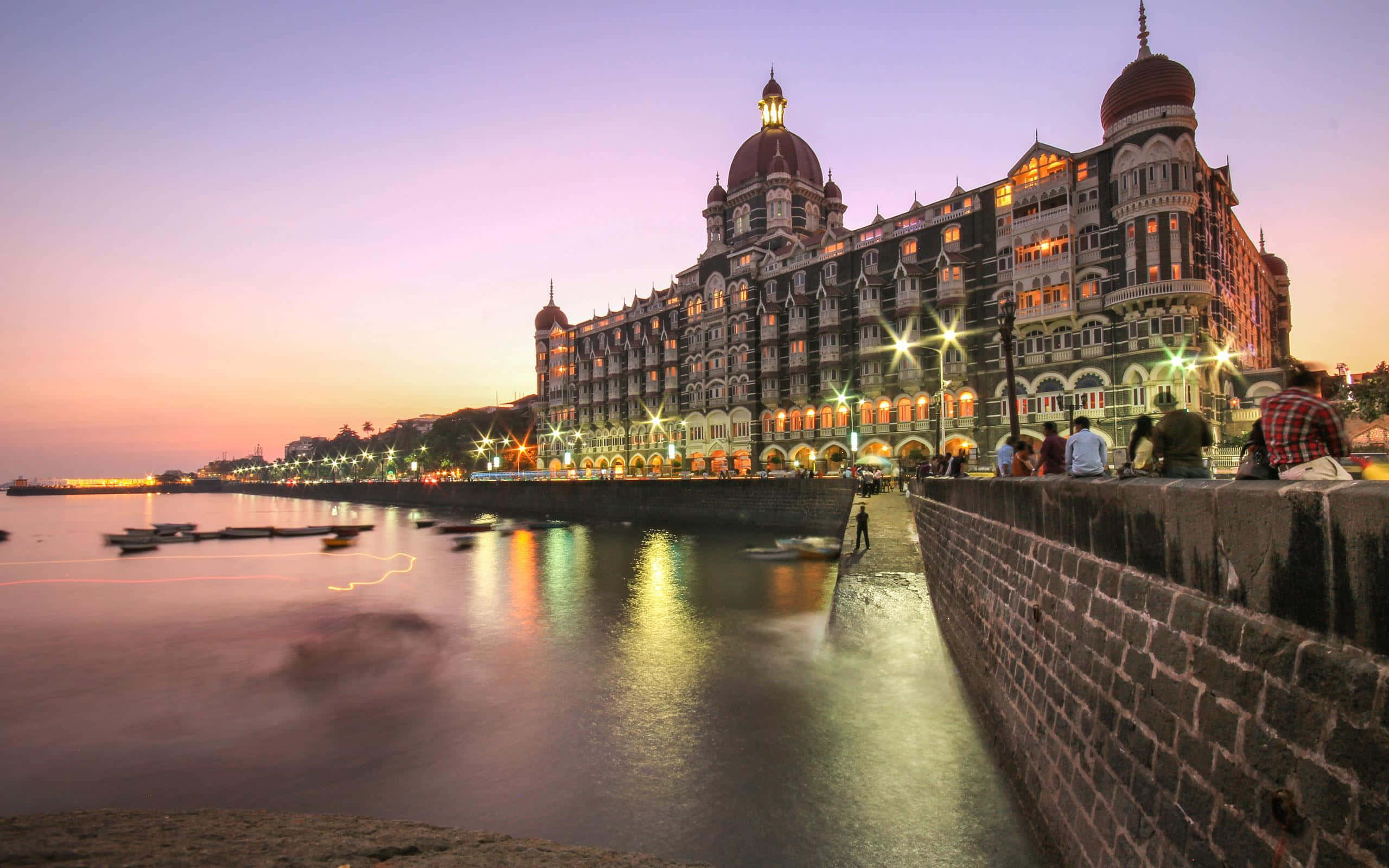 Mumbai 桌布 壁紙 — 泰姬瑪哈皇宮酒店在黃昏時散發溫暖光芒，其圓頂和拱門倒映在孟買海濱平靜的水面上。