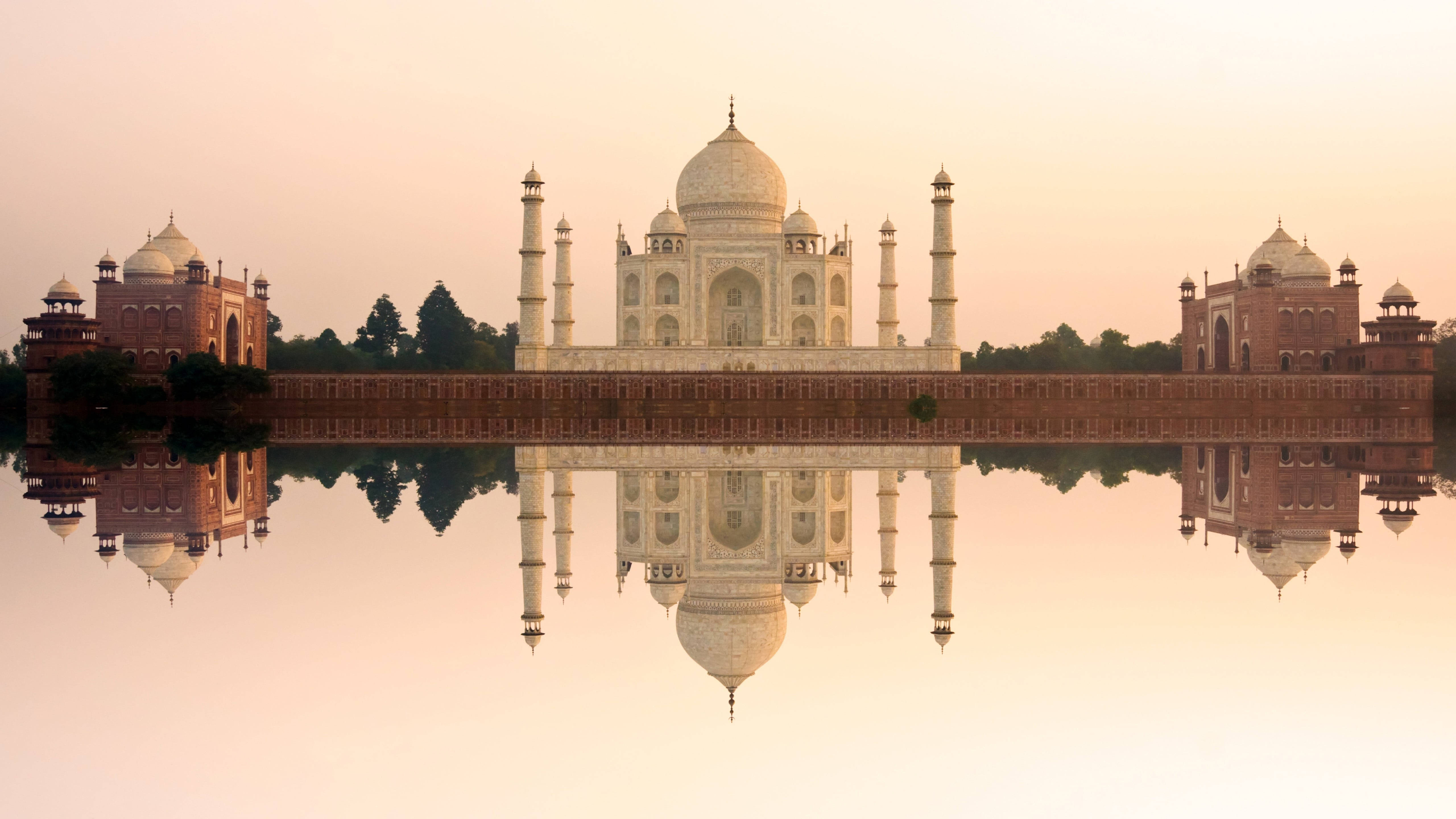 Delhi 桌布 壁紙 — 泰姬瑪哈陵在日出時靜靜矗立，平靜的水面完美倒映，四周環繞著柔和的粉紅與金色調。