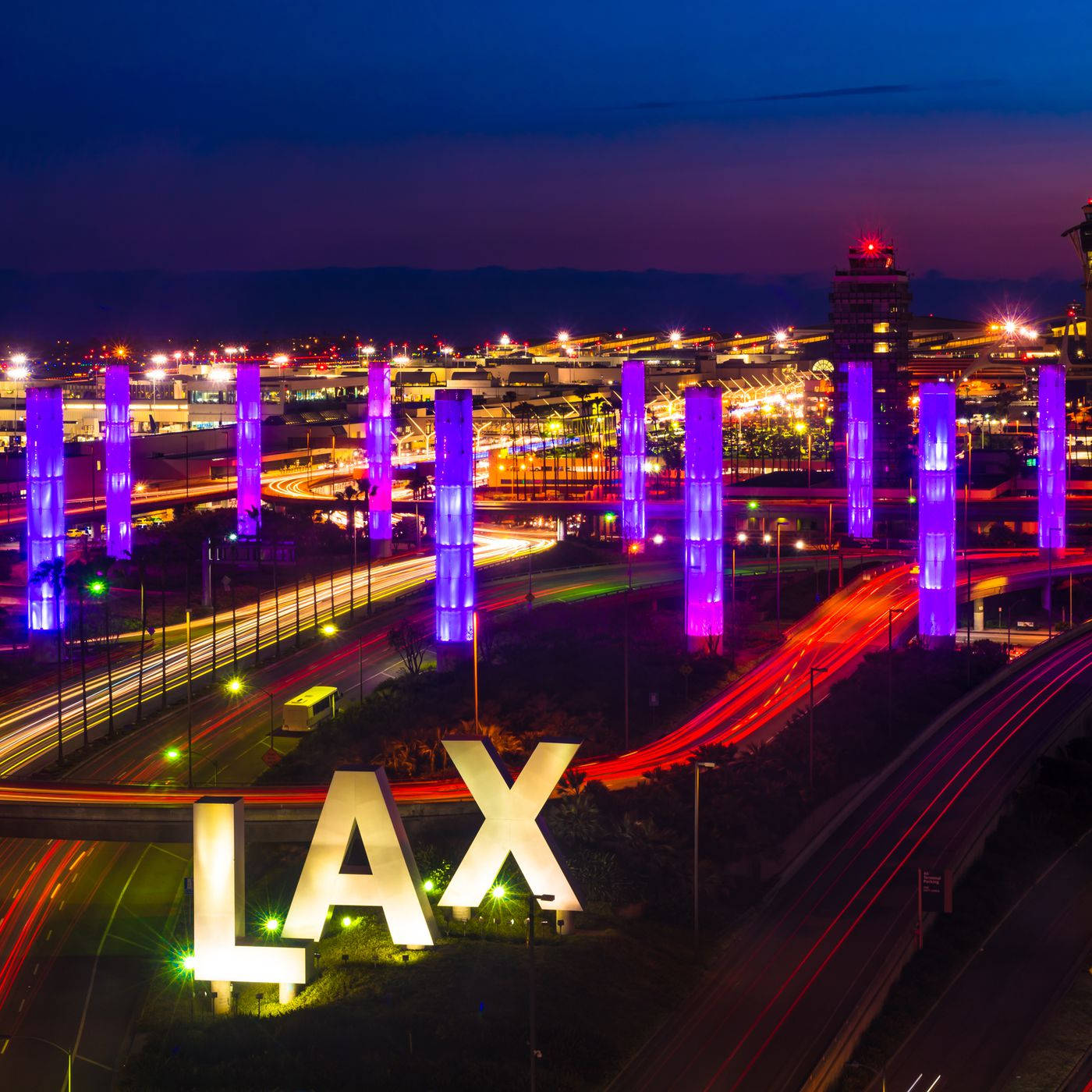 加州 桌布 壁紙 — 洛杉磯國際機場（LAX）充滿活力的夜景，紫色發光柱和車流的光跡，在深藍色的天空下。