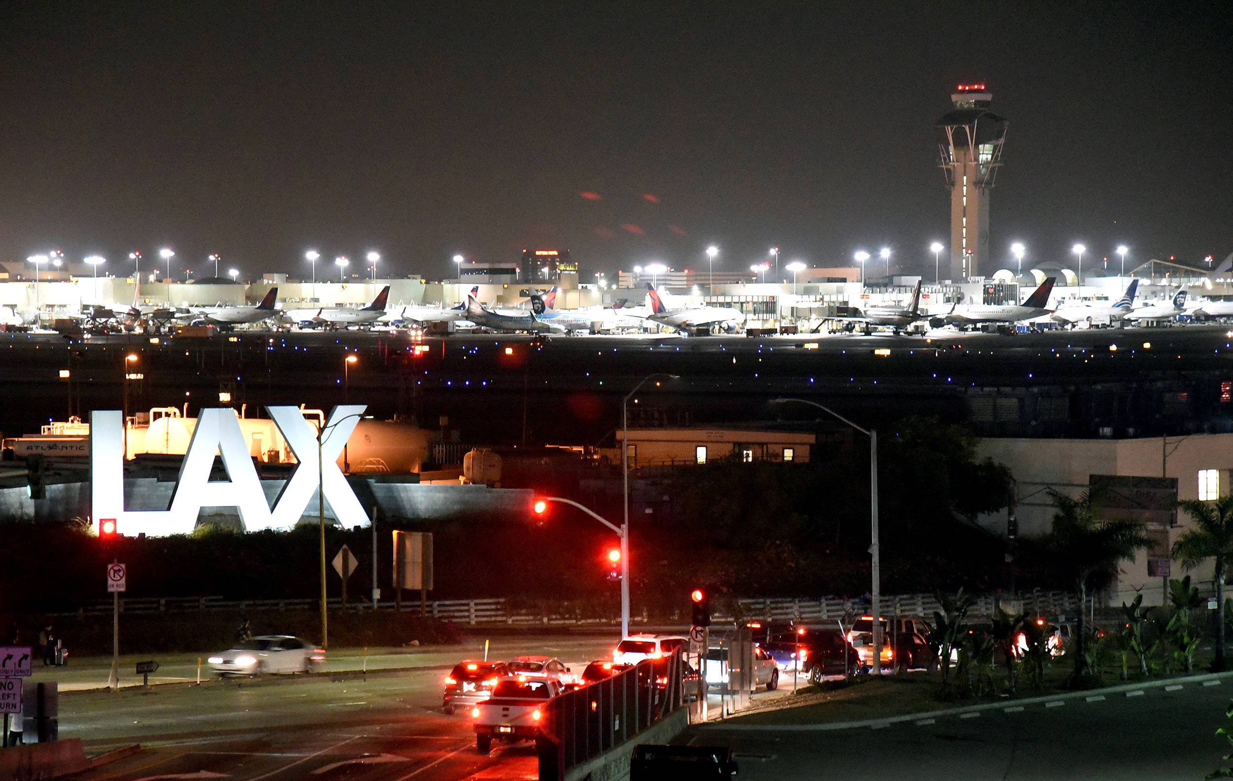加州 桌布 壁紙 — 洛杉磯國際機場夜景，發光標誌、停放在明亮燈光下的飛機以及下方流動的交通。