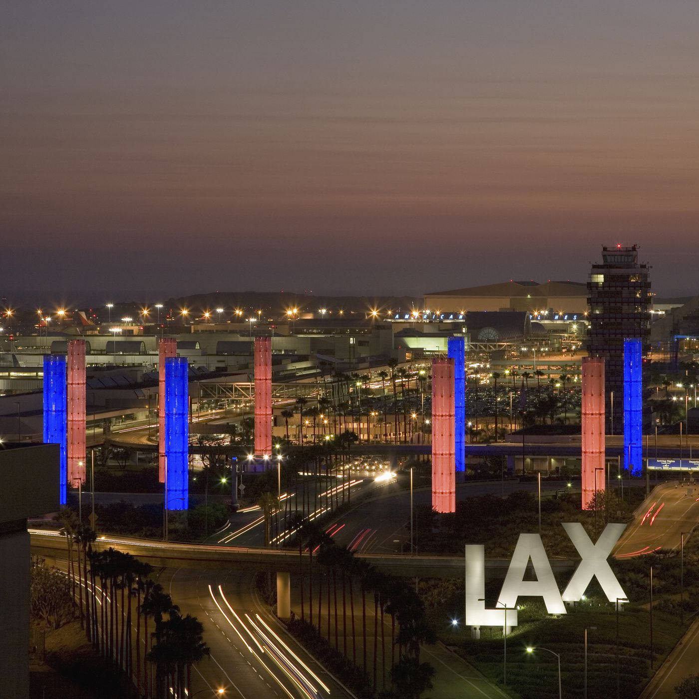 加州 桌布 壁紙 — 洛杉磯國際機場的黃昏景色，帶有發光的藍色和粉紅色柱子以及移動車輛的光跡。