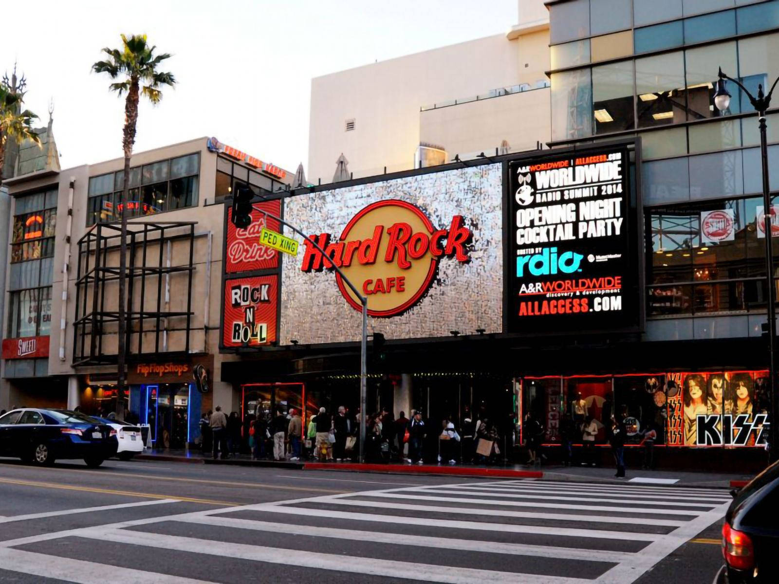 好萊塢街頭 桌布 壁紙 — 洛杉磯市中心，Hard Rock Cafe 店面在黃昏時閃耀，棕櫚樹和行人穿越街道。