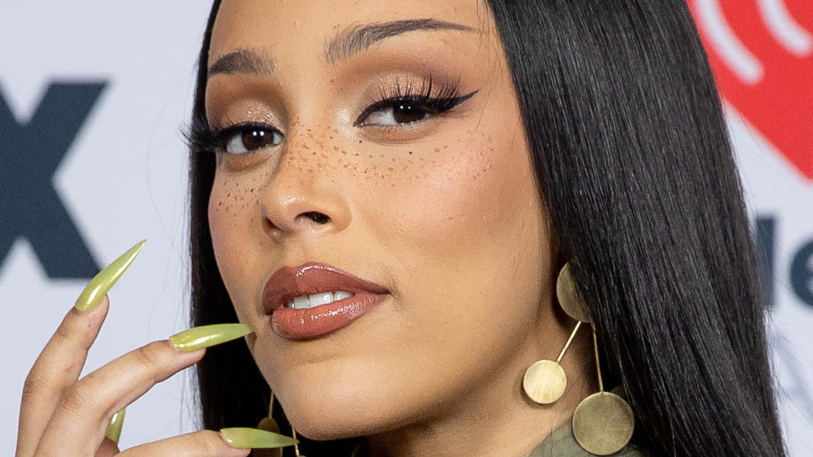 Doja Cat 桌布 壁紙 — 活動中擺姿勢的長黑髮、雀斑和綠色指甲女性的特寫肖像。