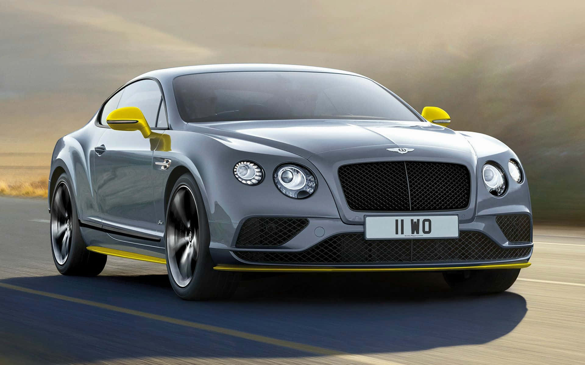 Best Bentley 桌布 壁紙 — 流線型銀色賓利 Continental GT 帶有醒目黃色點綴，在朦朧金色天空下於沙漠公路上疾馳。