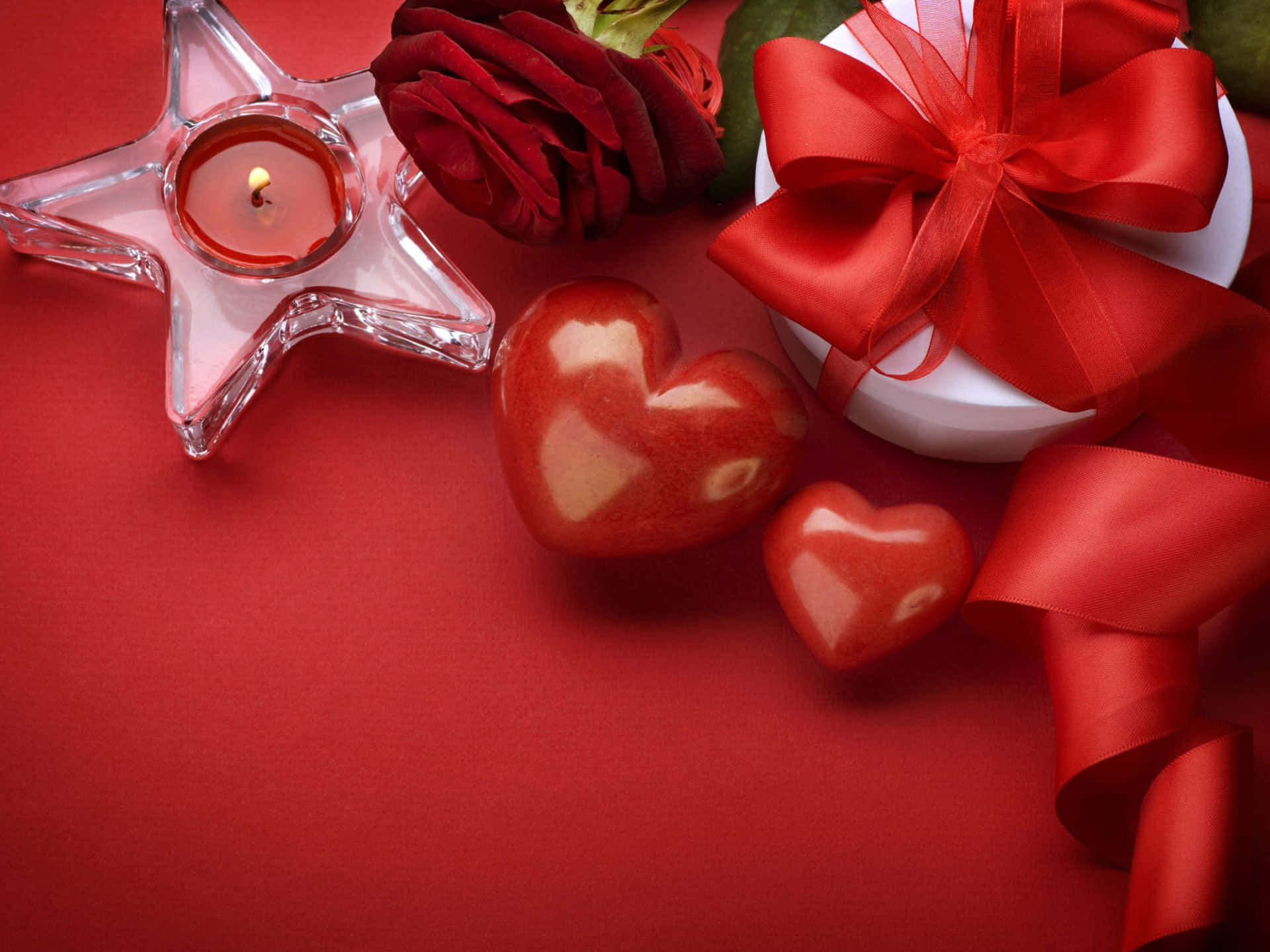 Rose Heart 桌布 壁紙 — 浪漫靜物畫，以紅玫瑰、點燃的星星蠟燭、心形裝飾和禮物蝴蝶結為特色，背景為濃郁的紅色。