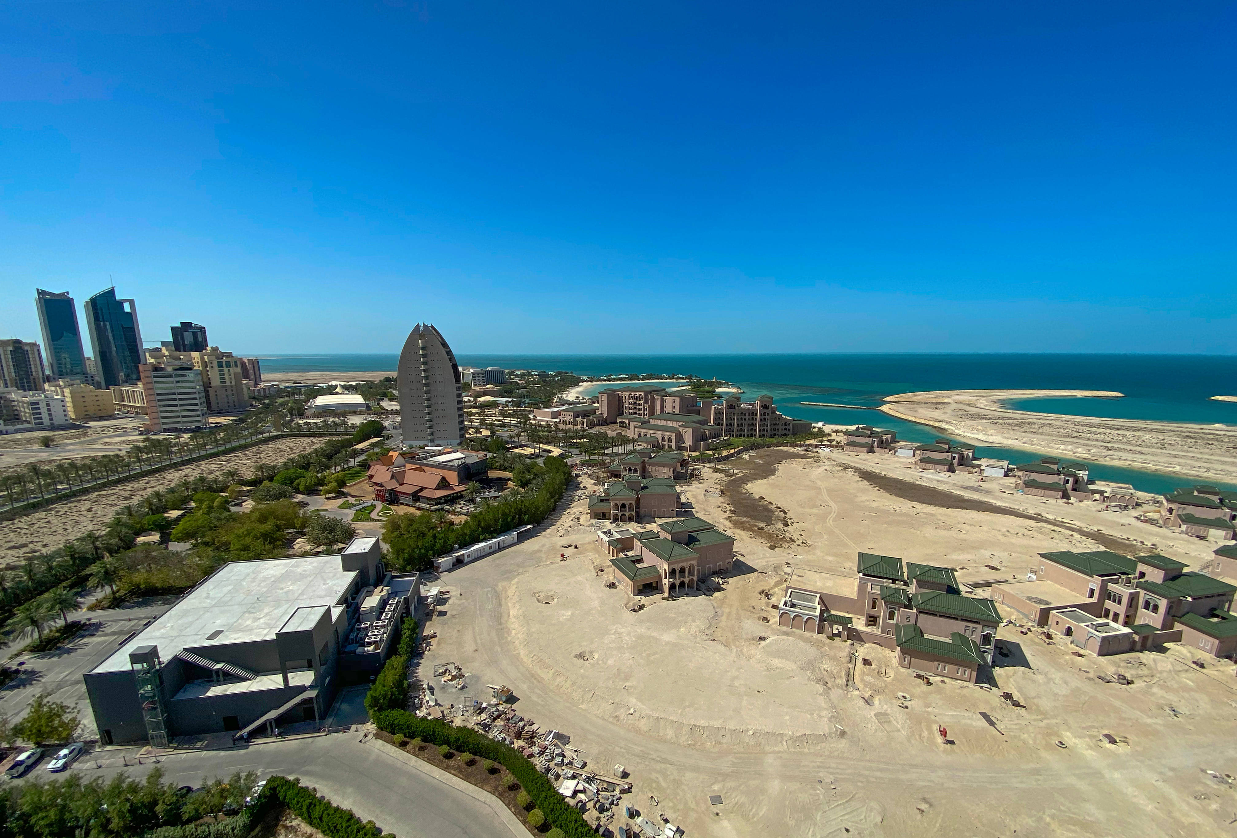Bahrain 桌布 壁紙 — 海岸城市天際線的鳥瞰圖，擁有現代摩天大樓和一座獨特的帆形酒店，旁邊是碧綠的海水和沙質建築區。