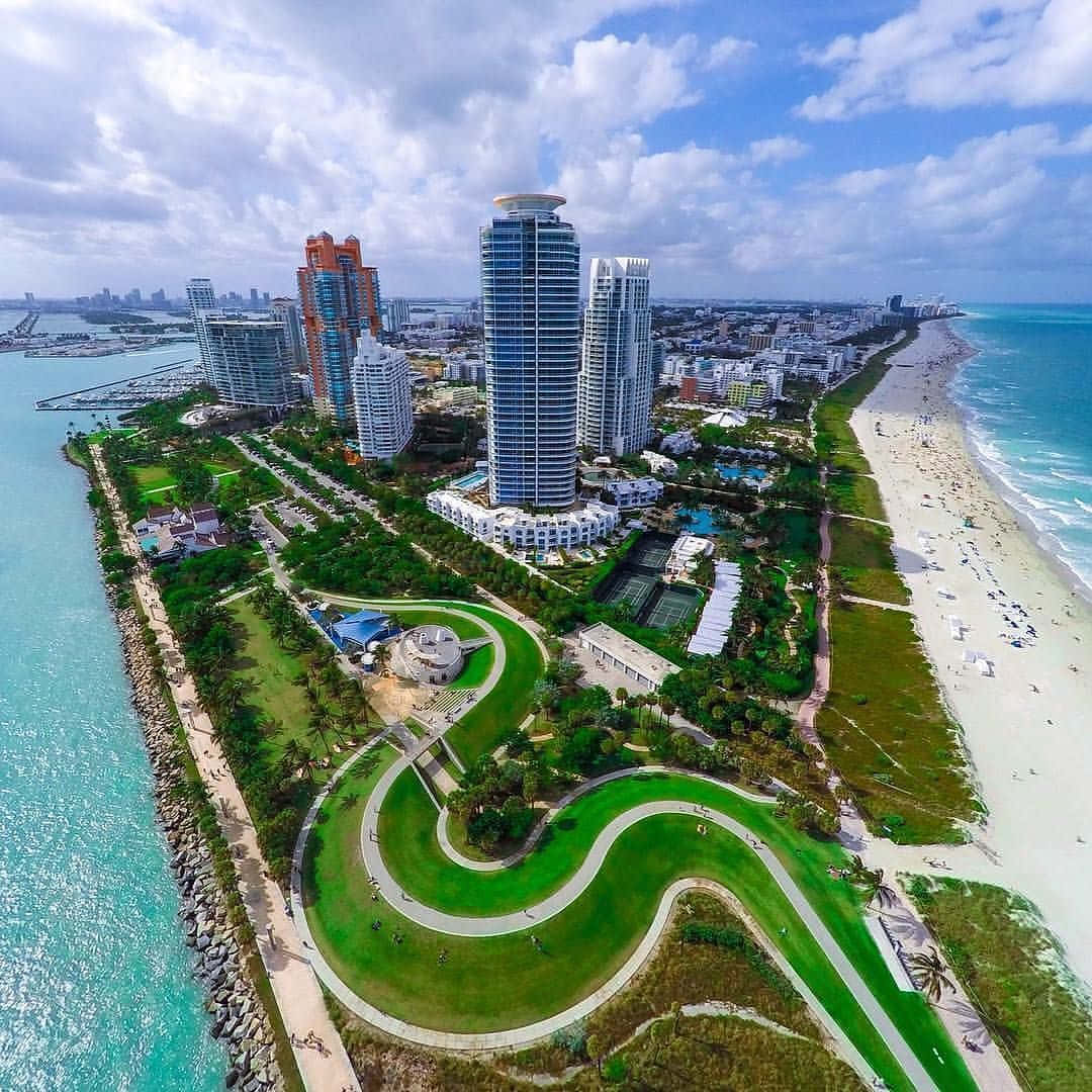 Miami 桌布 壁紙 — 海岸城市景觀的鳥瞰圖，擁有碧綠的海水、沙灘和現代摩天大樓，坐落在茂密的綠色公園之中。