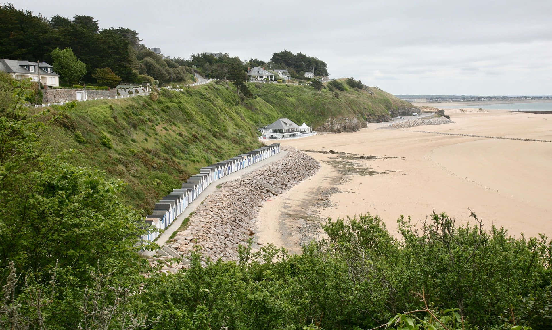 French Beach 桌布 壁紙 — 海岸景色，有沙灘、綠色懸崖，以及樹叢中隱藏的白屋，天空多雲。