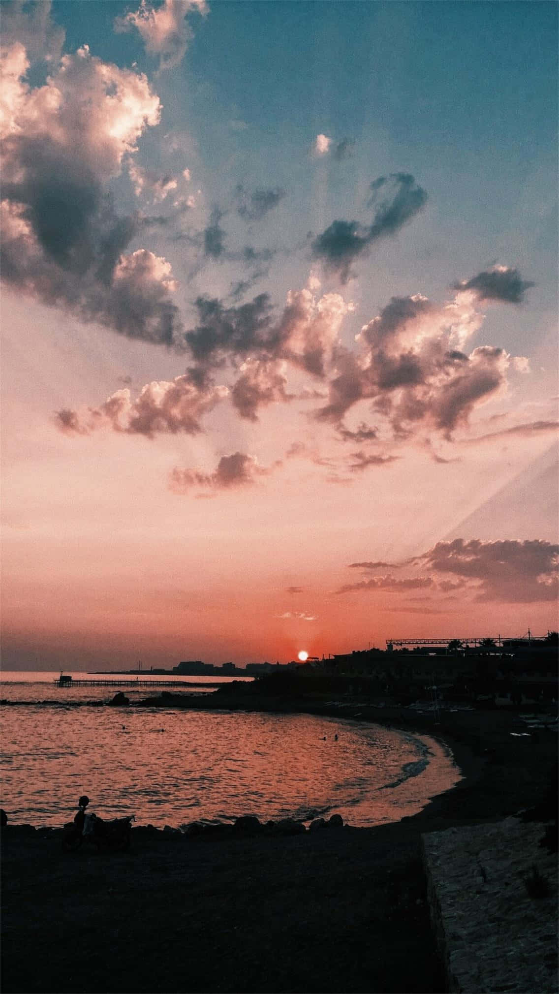 vsco 桌布 壁紙 — 海岸灣的寧靜日落，粉紅色和橙色的雲彩映照在平靜的水面和剪影般的懸崖上。