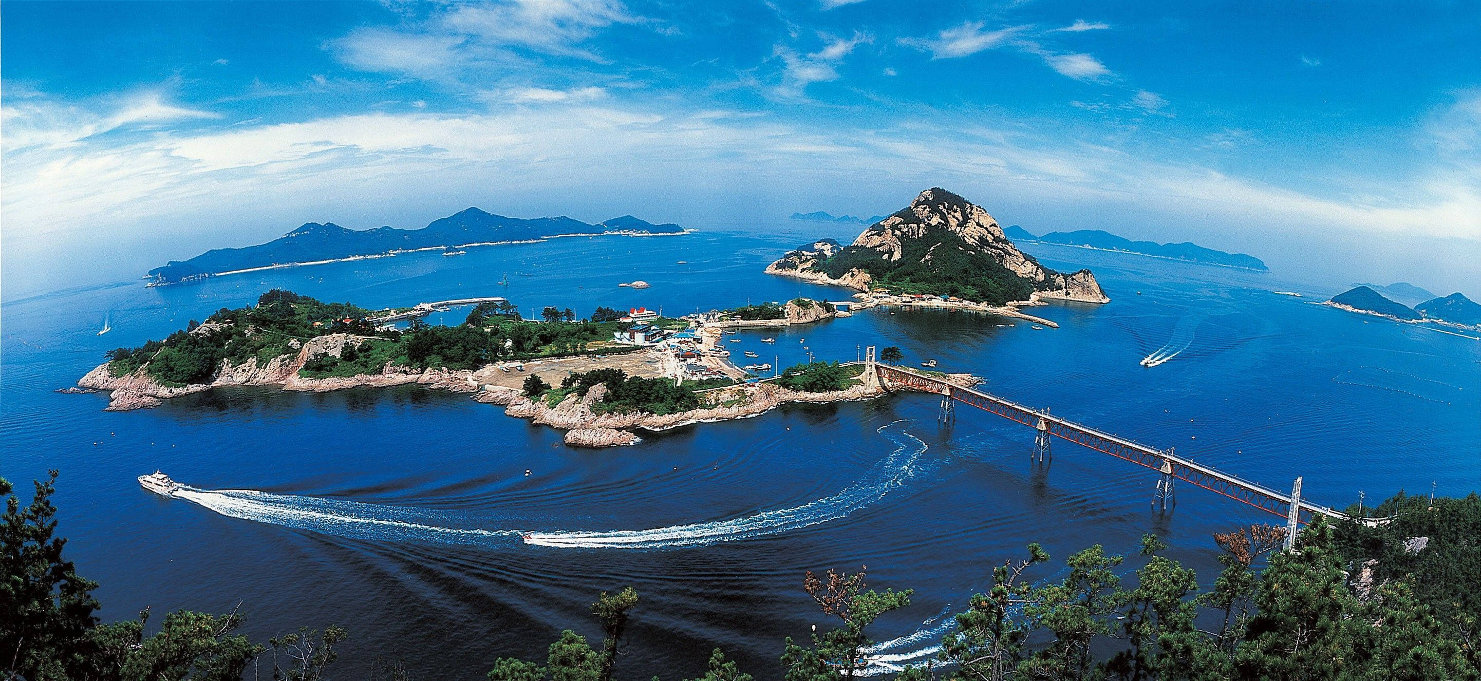 島嶼 桌布 壁紙 — 海岸群島的鳥瞰圖，碧綠的海水，船隻飛馳，一條長橋連接崎嶇的綠色島嶼，天空湛藍。