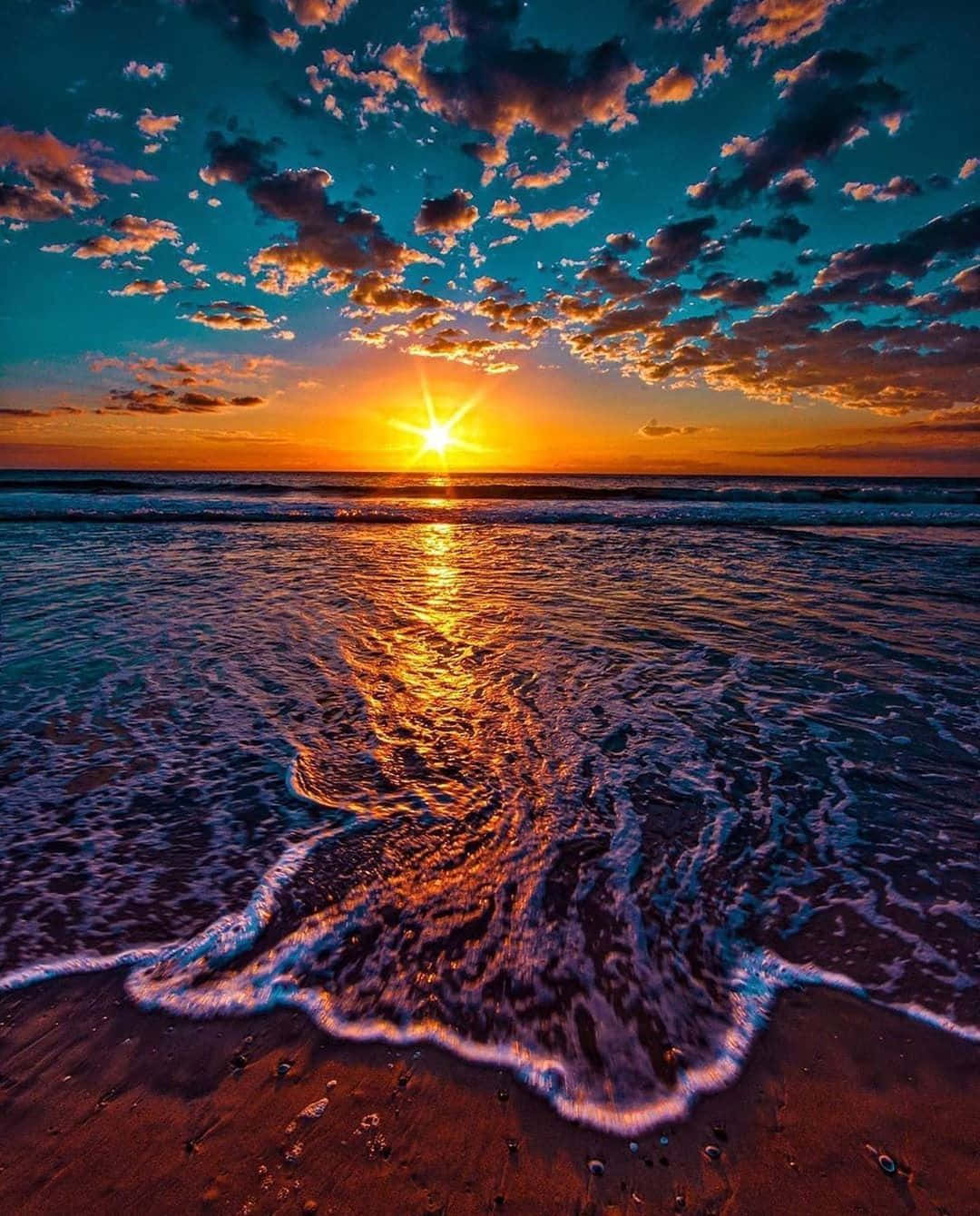 桌布 壁紙 — 海洋上充滿活力的日落，金色光線反射在泡沫海浪上，沖刷到沙灘上。