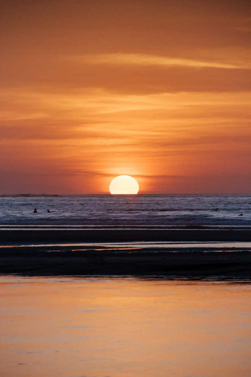 海灘 桌布 壁紙 — 海洋上寧靜的日落，發光的太陽在水面和天空上投射溫暖的橙色光芒。