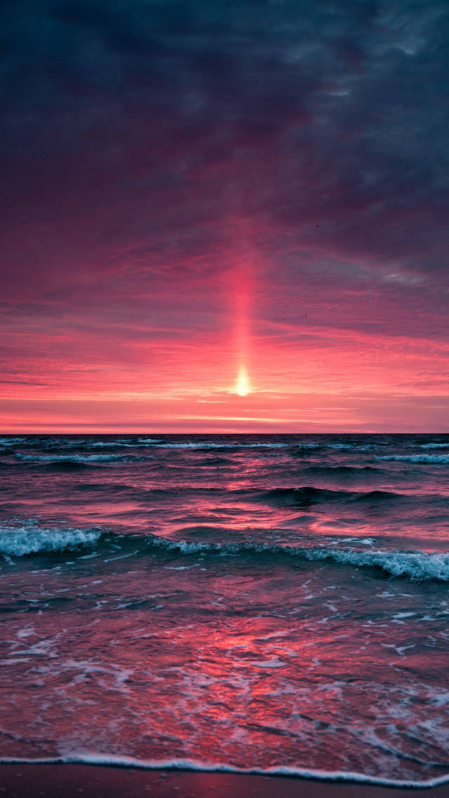 Pink Sunset iPhone 桌布 壁紙 — 海洋上戲劇性的日落，燦爛的太陽在海浪和天空中投射出鮮豔的粉紅色和紫色光芒。